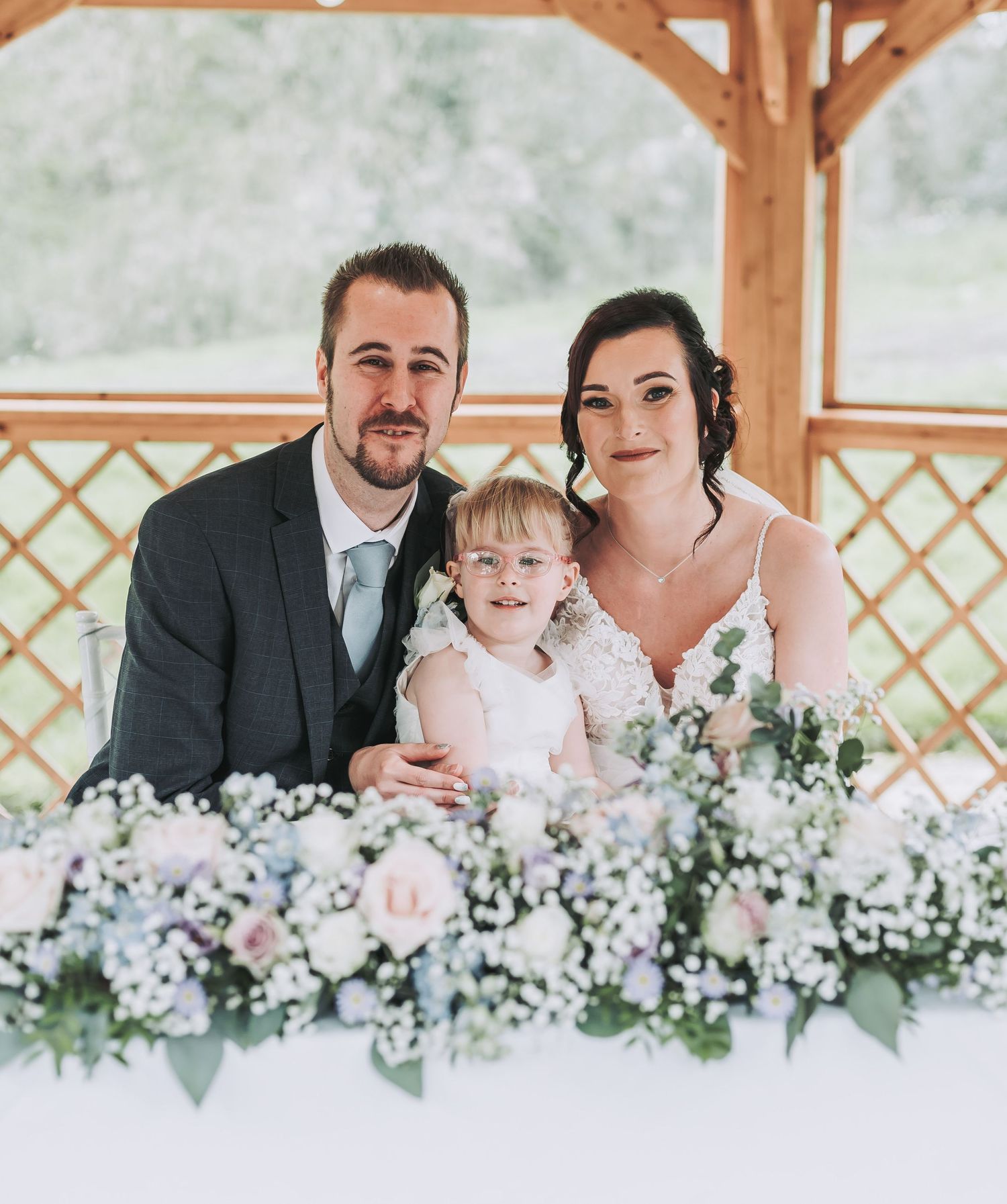 Wedding party poses together in a rustic gazebo with beautiful floral arrangements on the table.