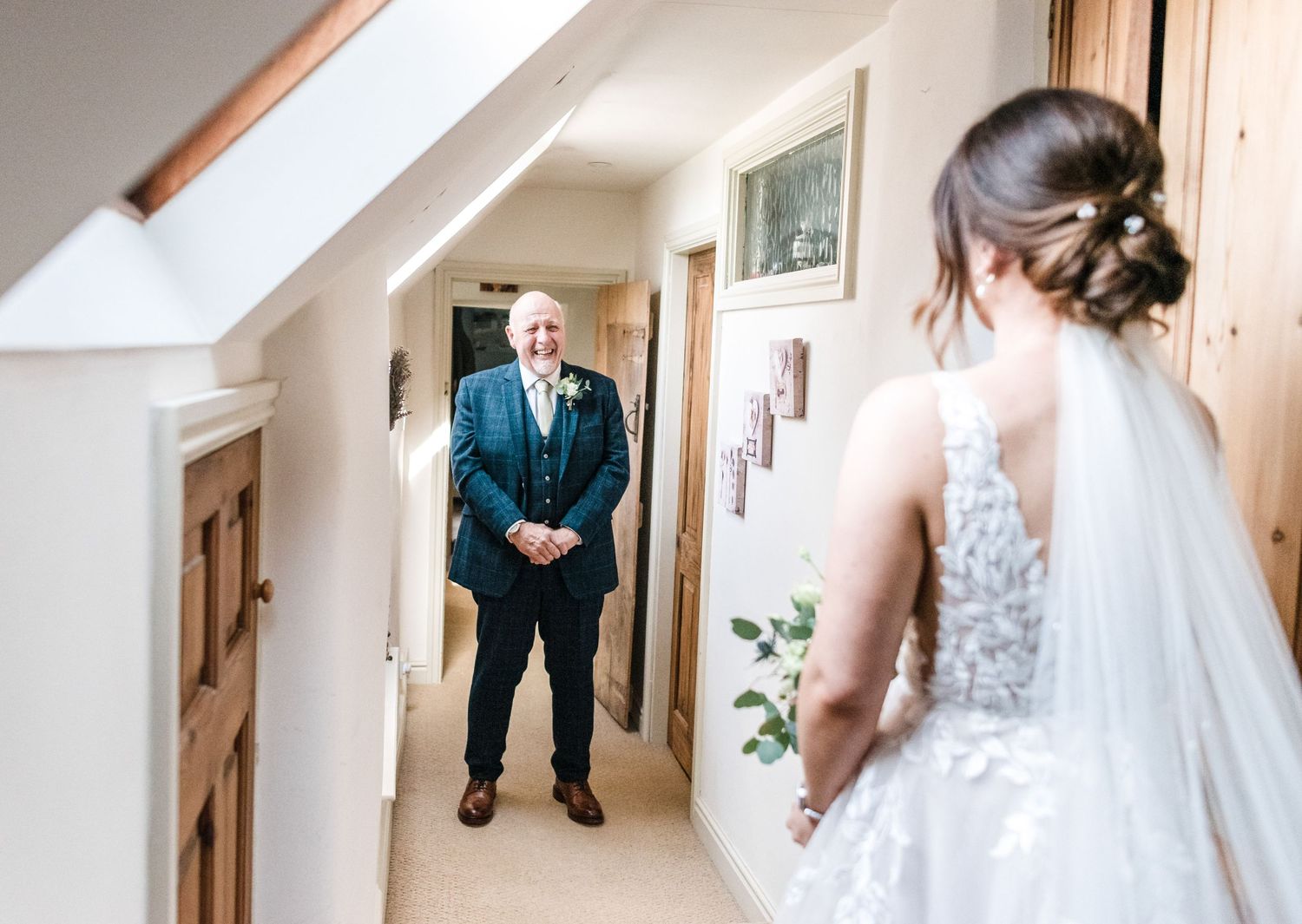 Emotional first look moment between bride and father in sunlit hallway.