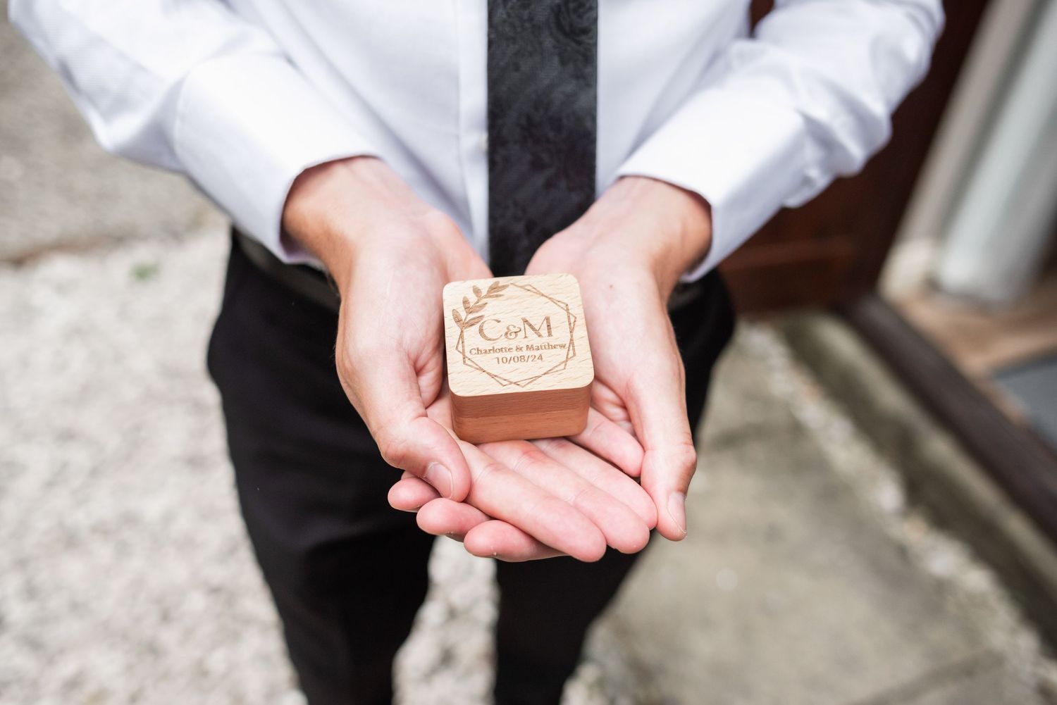 A pair of hands holding a small wooden box with a wedding ring stamp or seal.