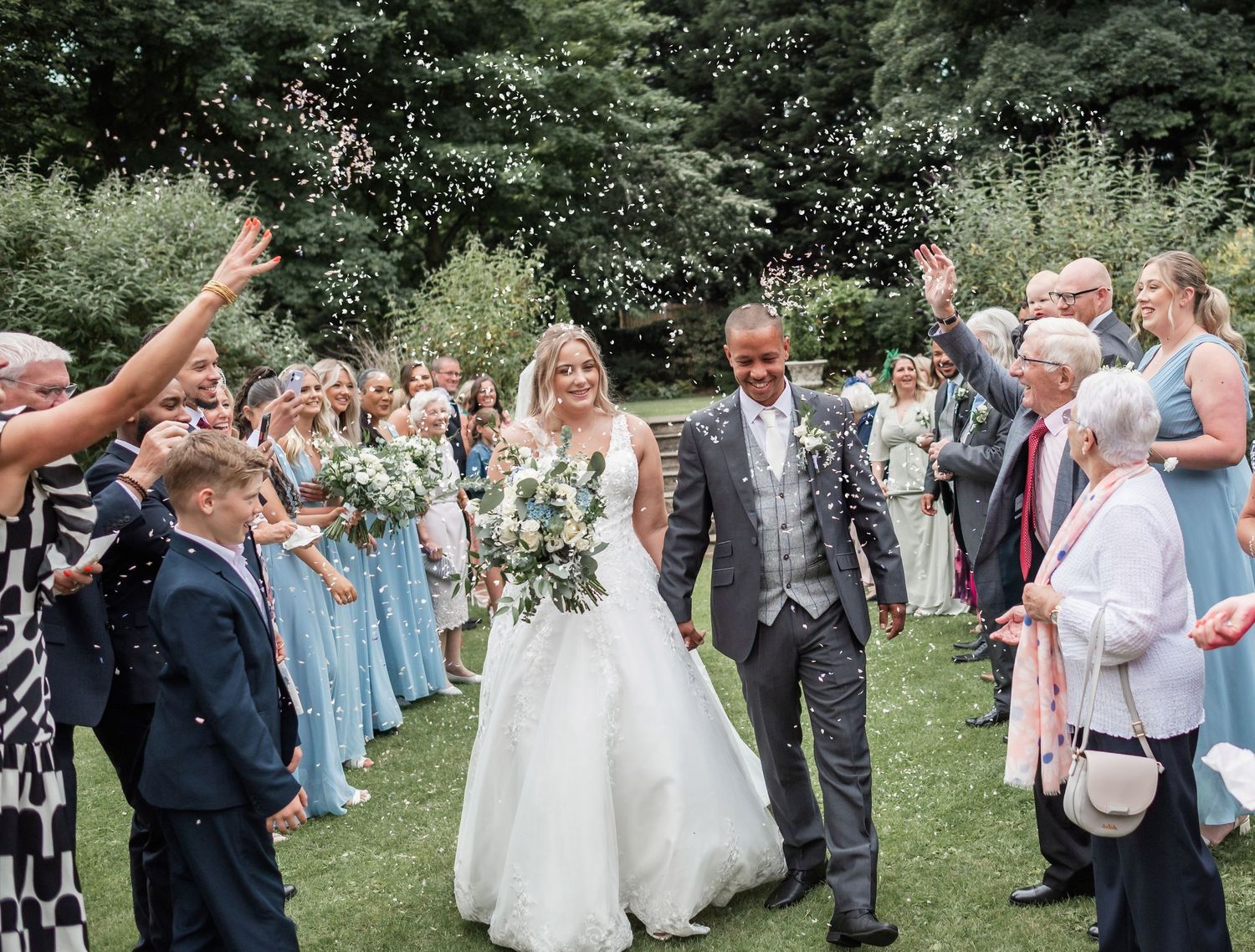 Wedding celebration outdoors with guests in blue dresses throwing confetti.
