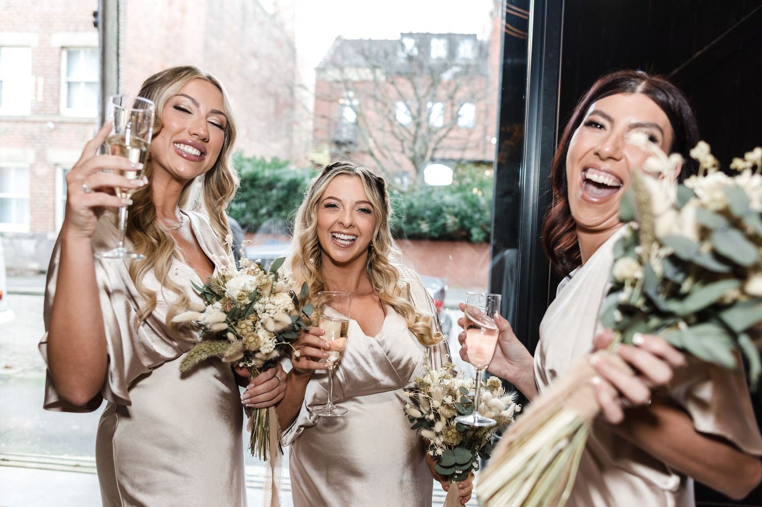 Bridesmaids in champagne dresses celebrating with bouquets and drinks.