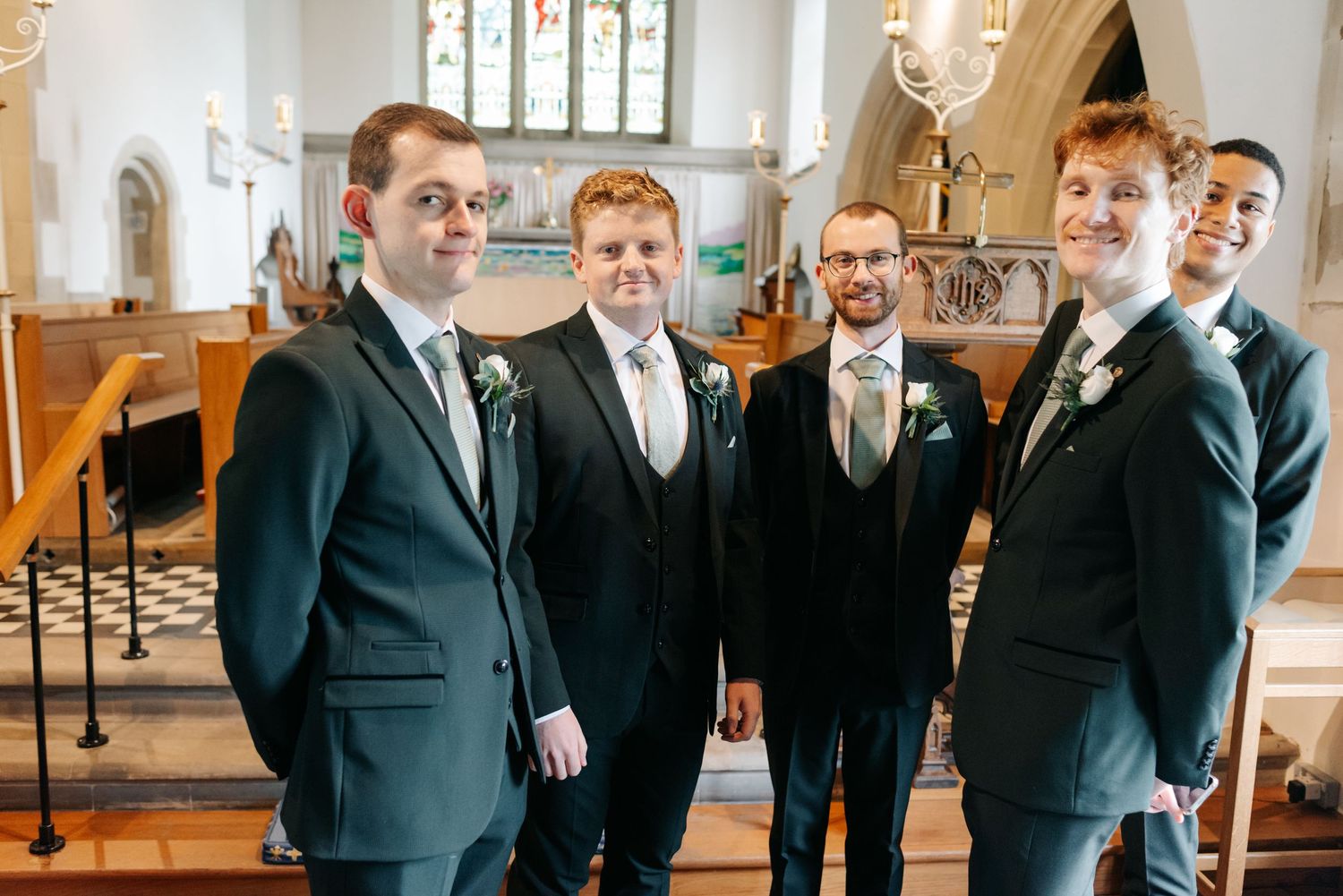 Groomsmen in dark suits share laughter and candid moments while getting ready for a wedding ceremony.