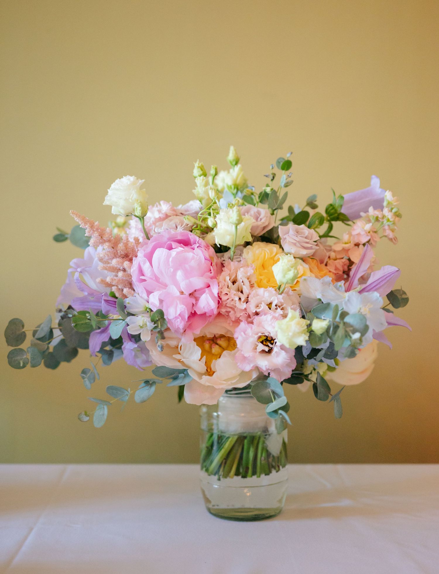 A sequence of delicate pink and peach floral arrangements with eucalyptus in glass vases against a beige background.