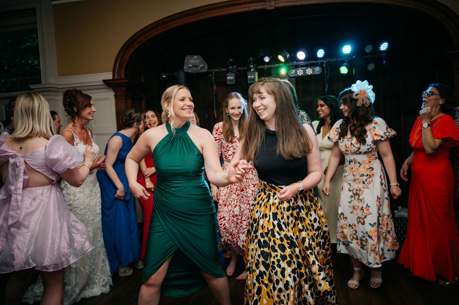 Wedding guests dancing and celebrating on a dimly lit dance floor with colorful party lights.