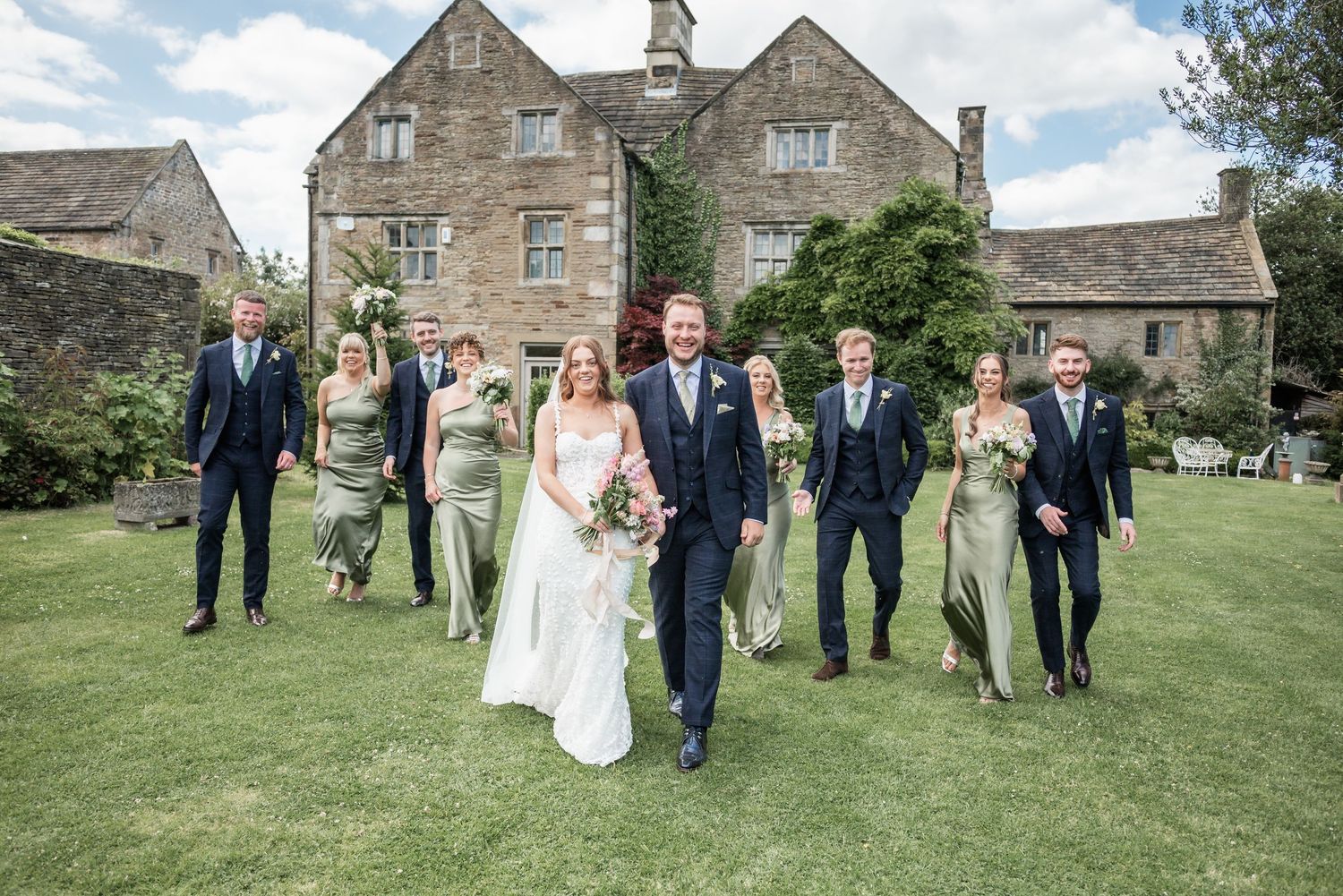 Wedding party and guests gathered outside traditional stone buildings.