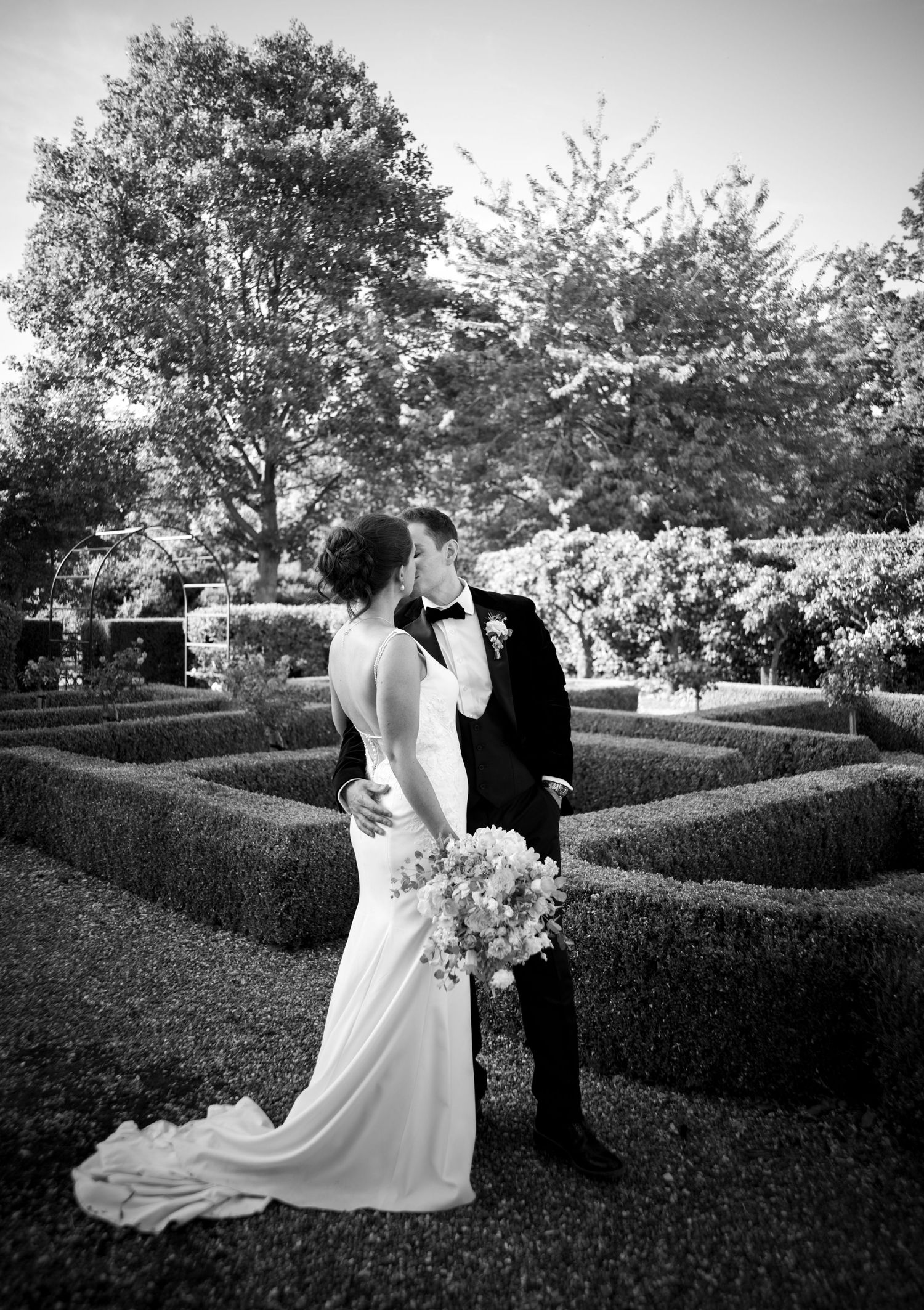 Black and white photos of wedding couple in formal garden with manicured hedges.