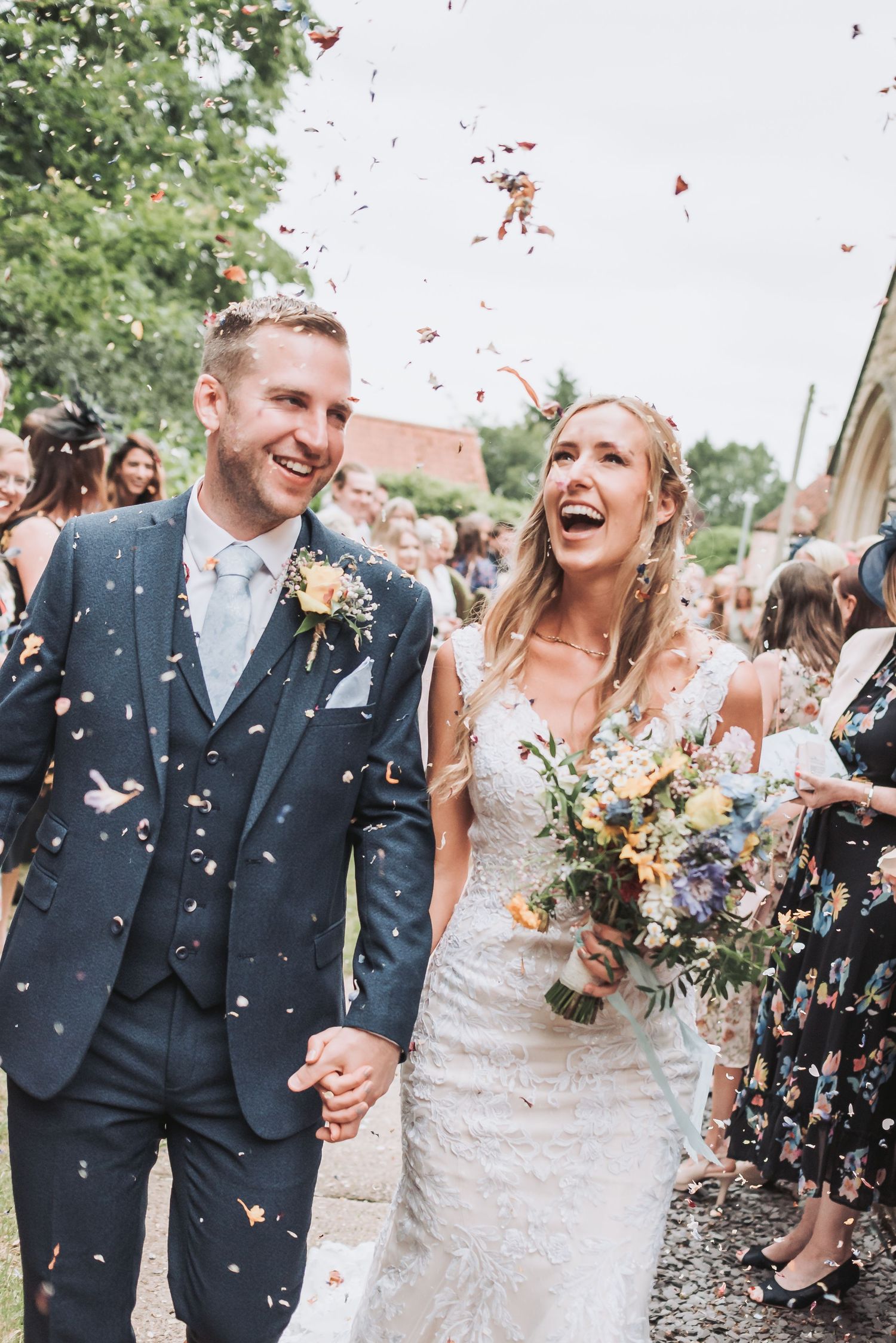 Joyful wedding celebration with confetti being thrown in an outdoor garden setting.