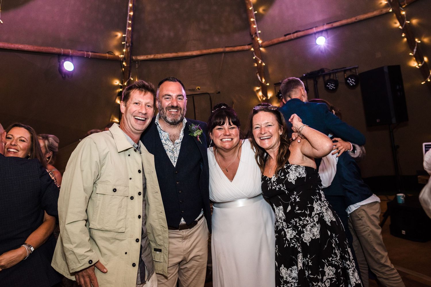 Wedding celebration with guests posing together under string lights in a tent venue.