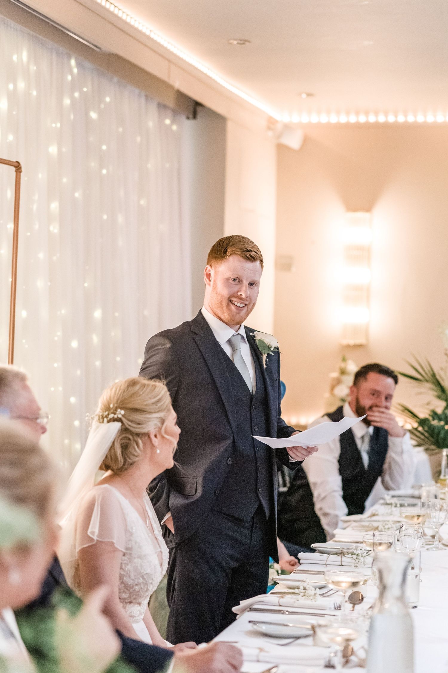 A wedding reception scene with fairy light backdrop and formal table settings.