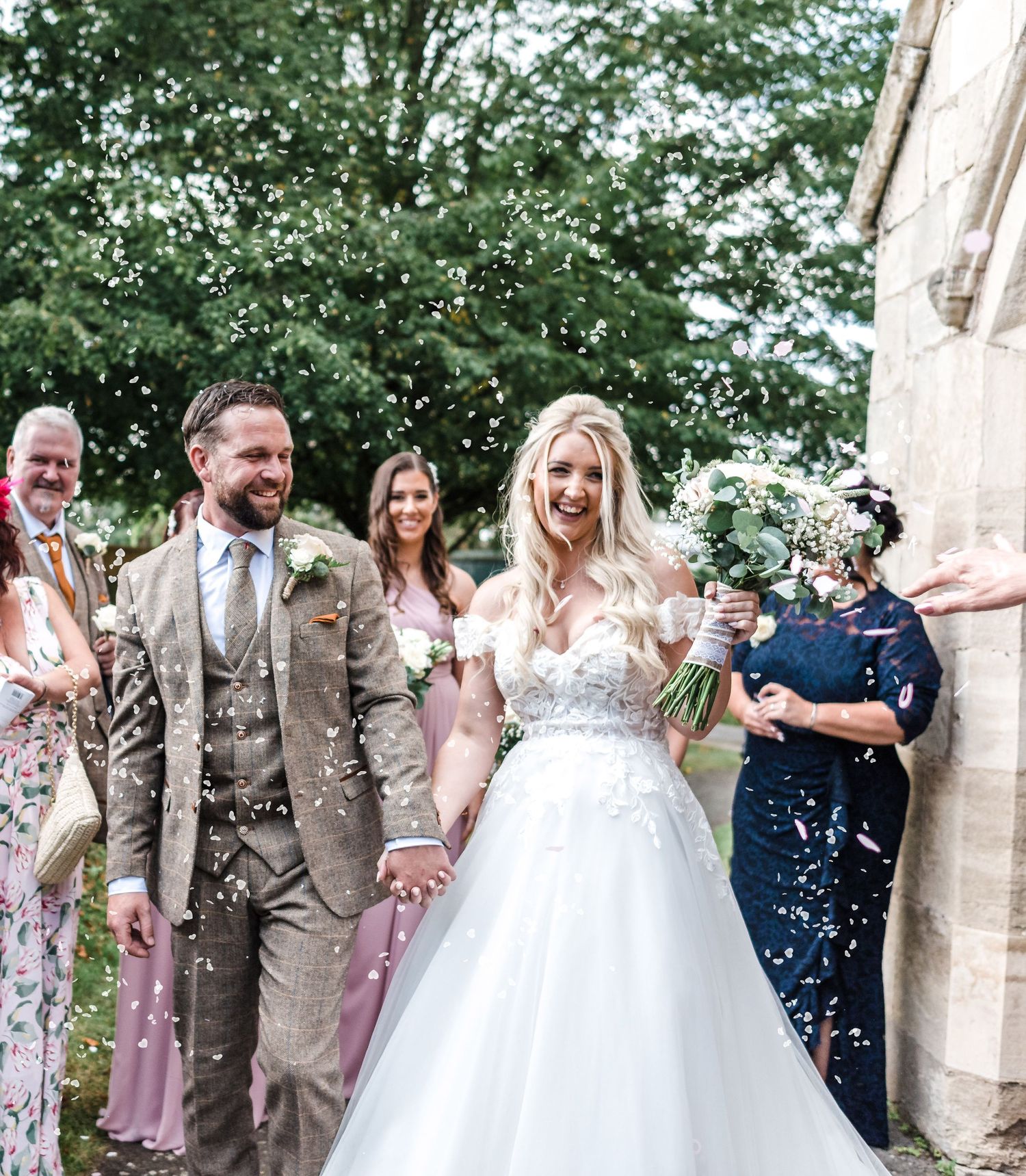 Wedding party celebrates with confetti outside a church on a sunny day.