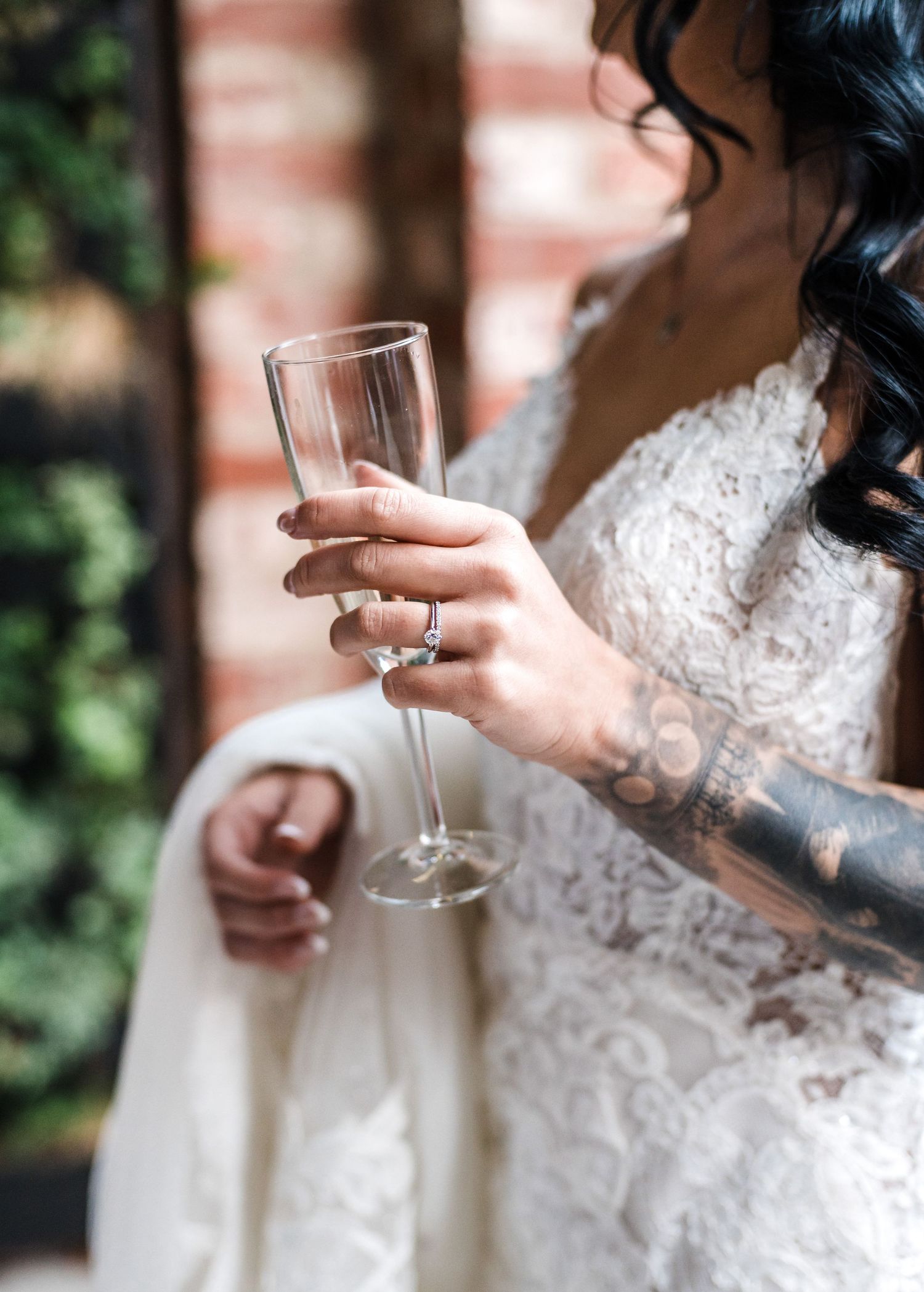 Close-up of champagne glass held by bride showing lace dress detail and ring.