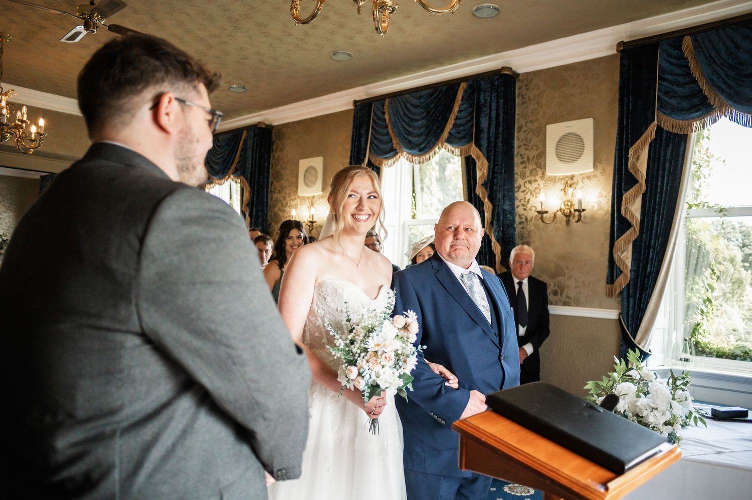 Indoor wedding ceremony in progress at elegant venue with navy curtains and chandeliers.