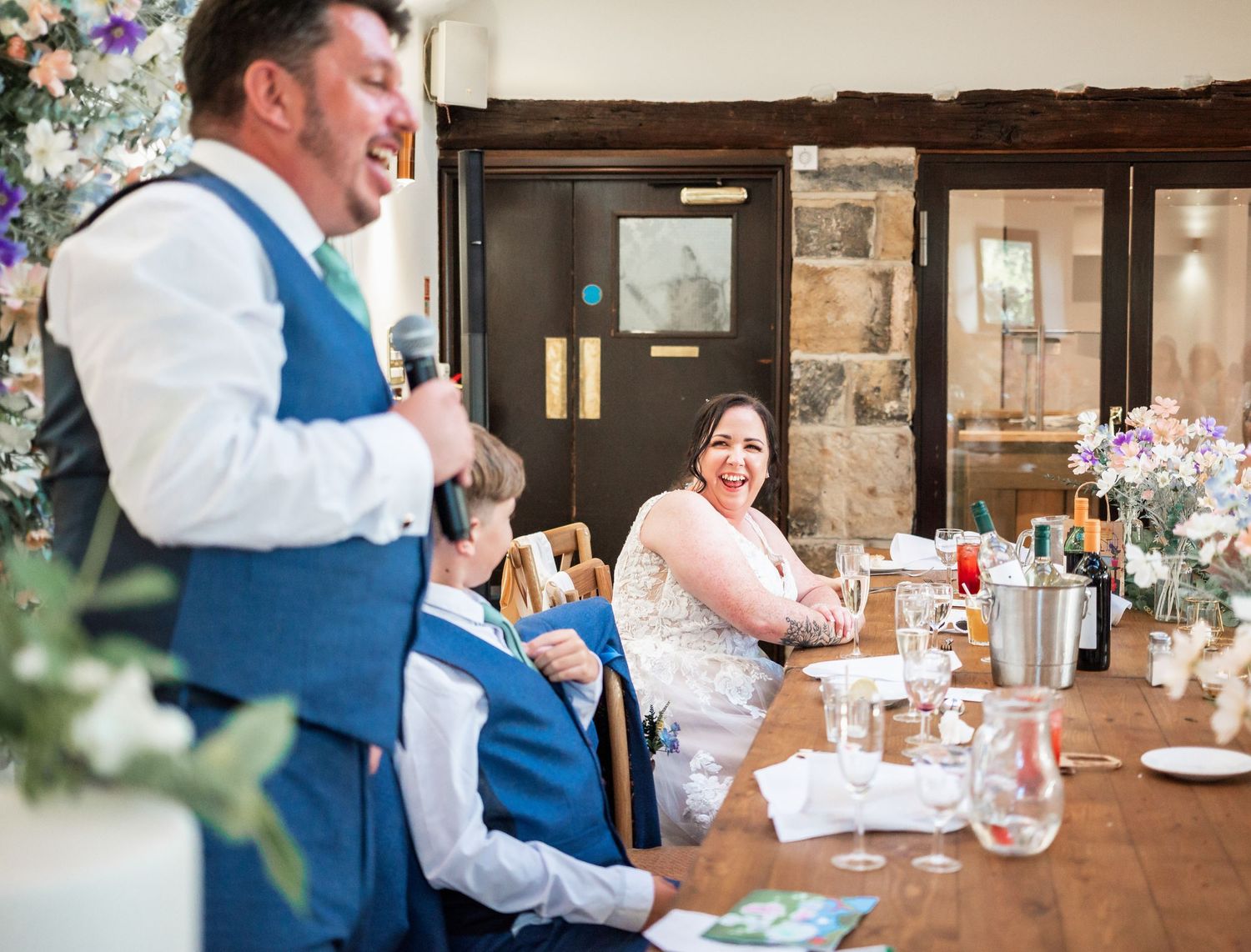 Reception speech moment captured during wedding dinner in rustic venue with floral decorations.