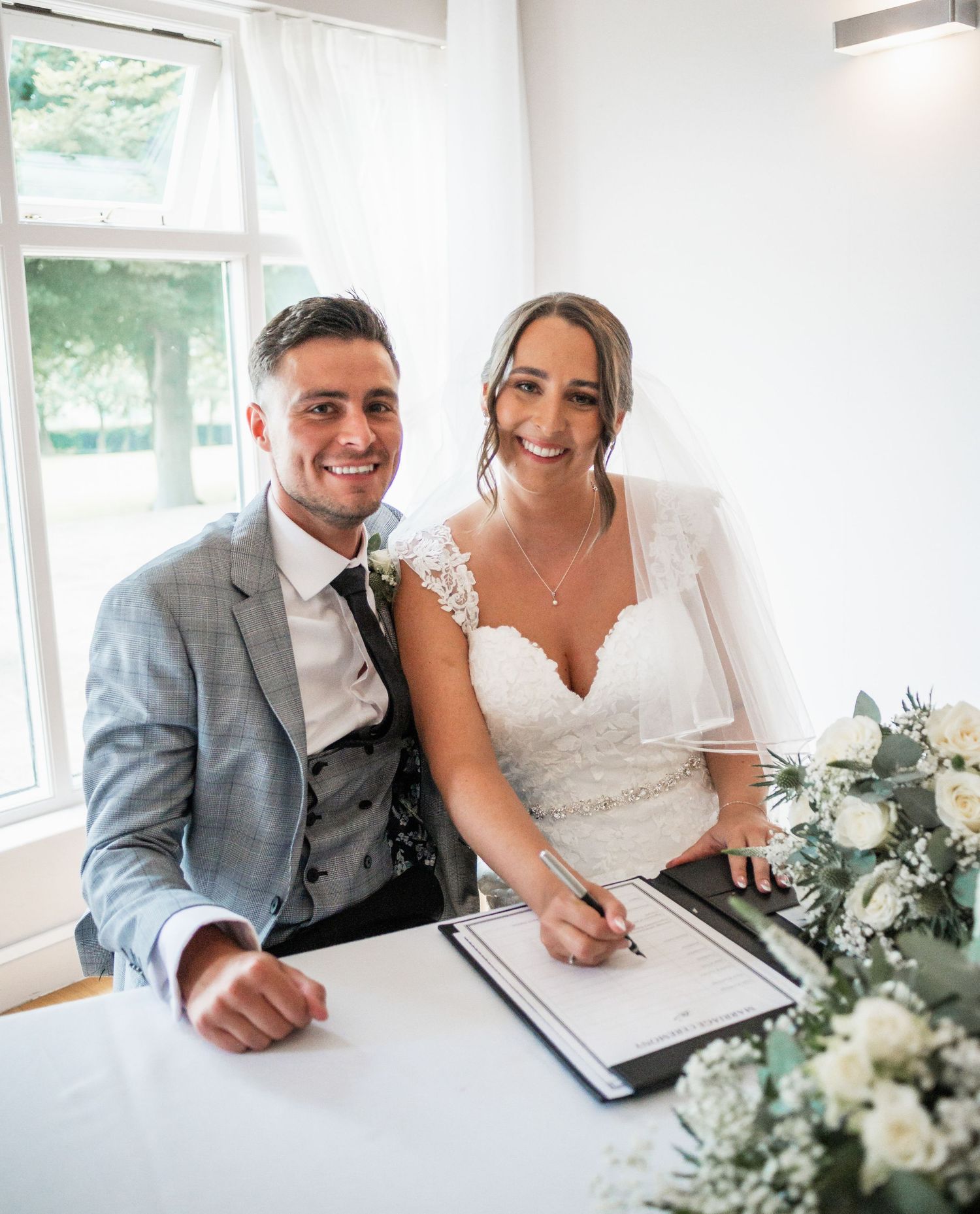 A signing ceremony at a wedding with floral decorations and bright interior.