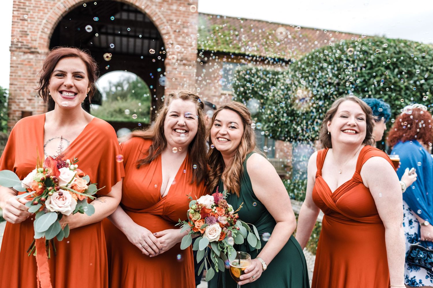 Bridesmaids in orange dresses share laughs during outdoor wedding celebration.