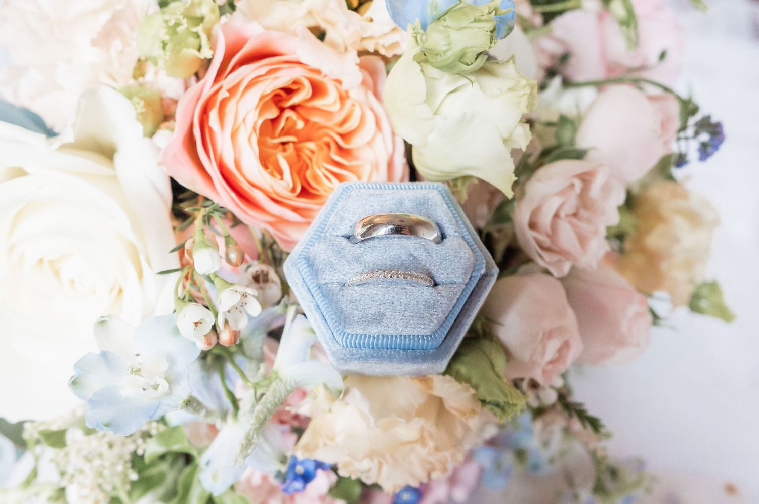 Close-up of a pale blue hexagonal ring box nestled among soft pink and white flowers.