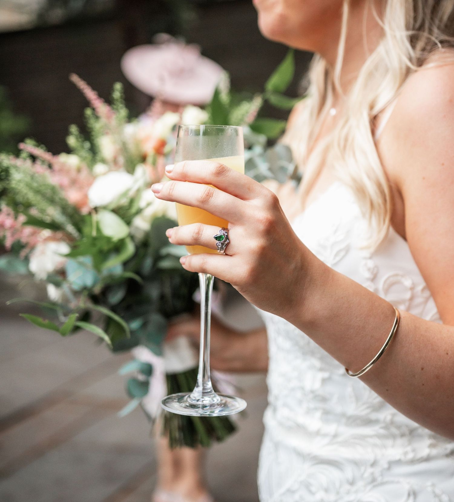 Close-up of bride holding champagne glass with floral arrangements in background.