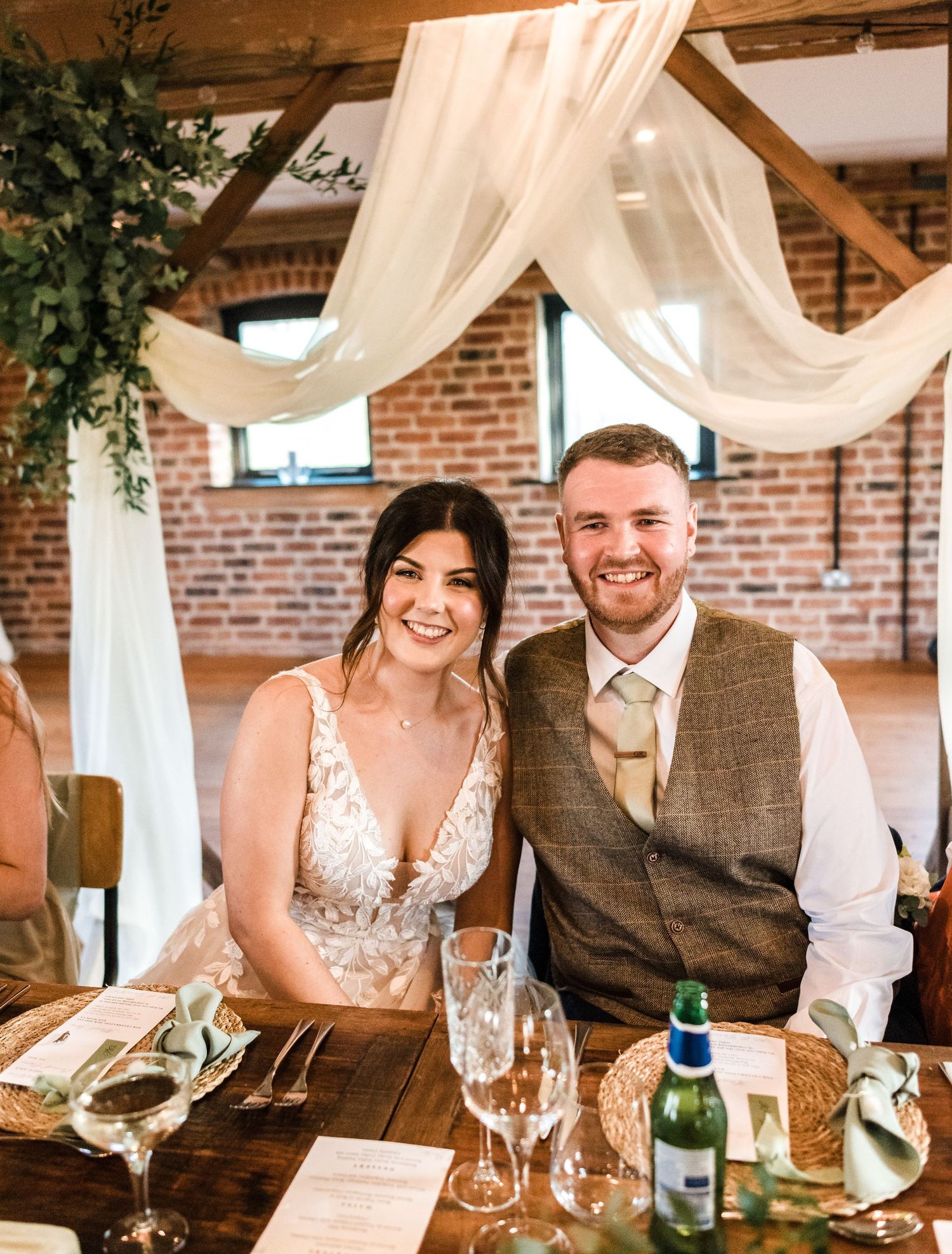 Wedding reception setup in rustic venue with white draping and exposed brick walls.