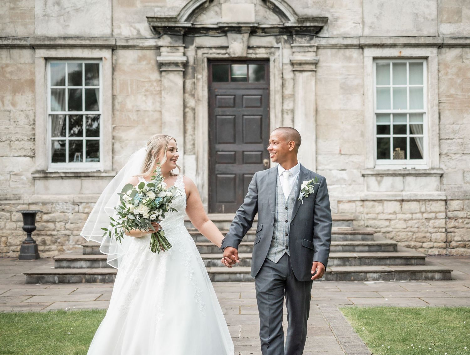 Couple poses in front of historic stone building on their wedding day.