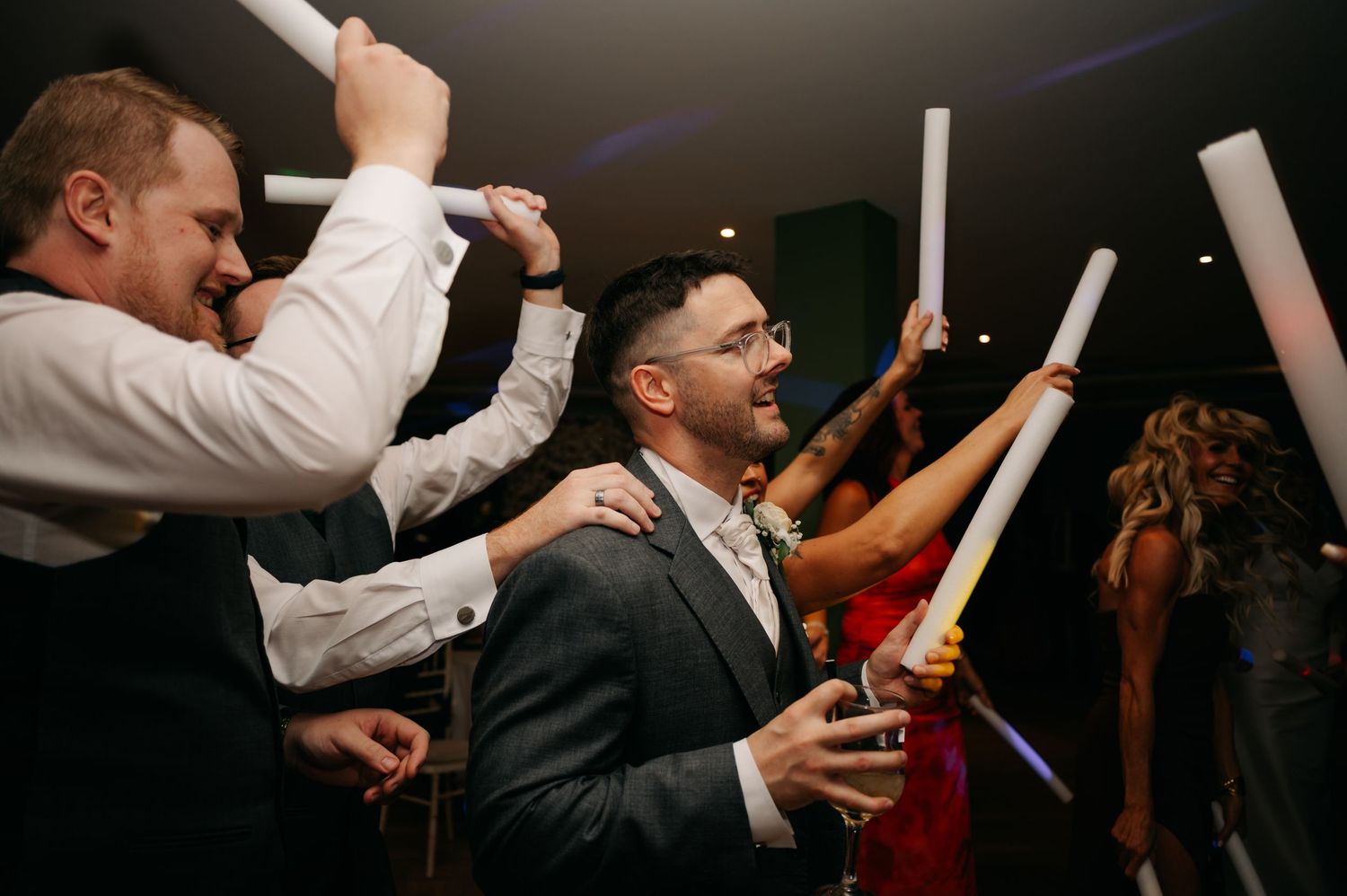 Wedding party celebrates on the dance floor with raised hands during evening reception.