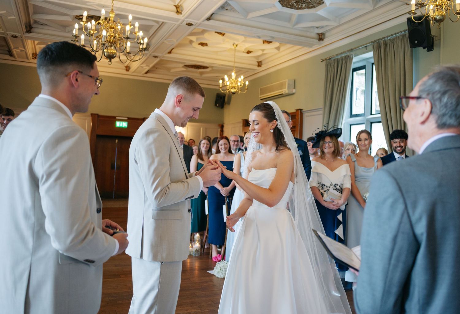 Wedding guests gather in an elegant ballroom with chandeliers for a celebration.