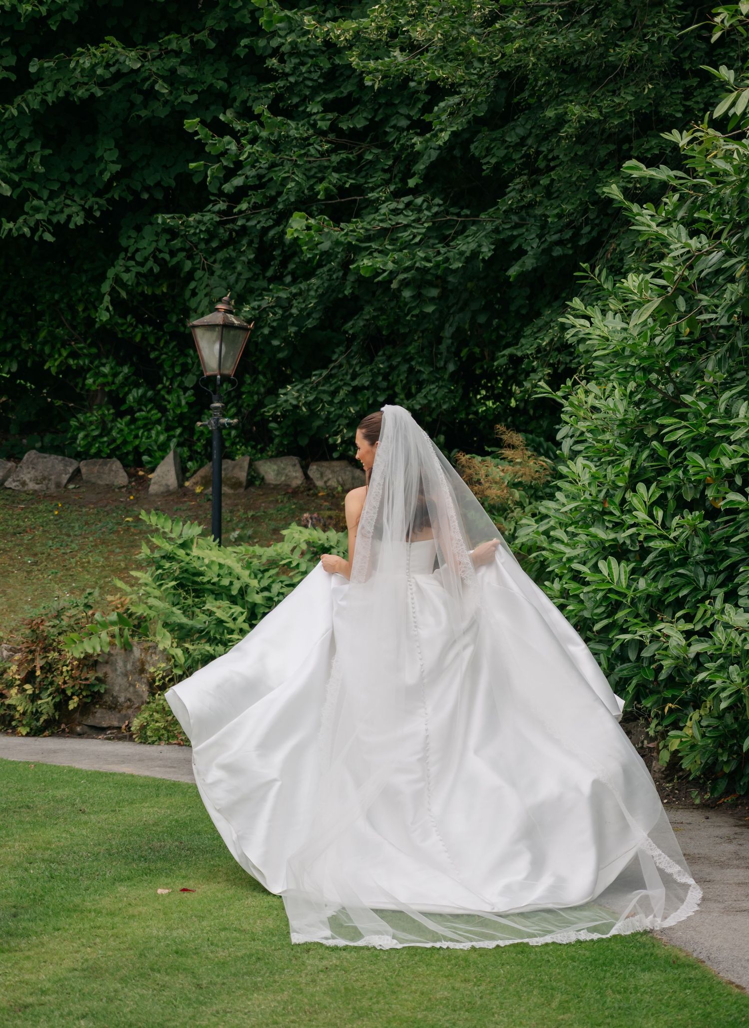 Flowing white wedding dress train trailing along a garden path.