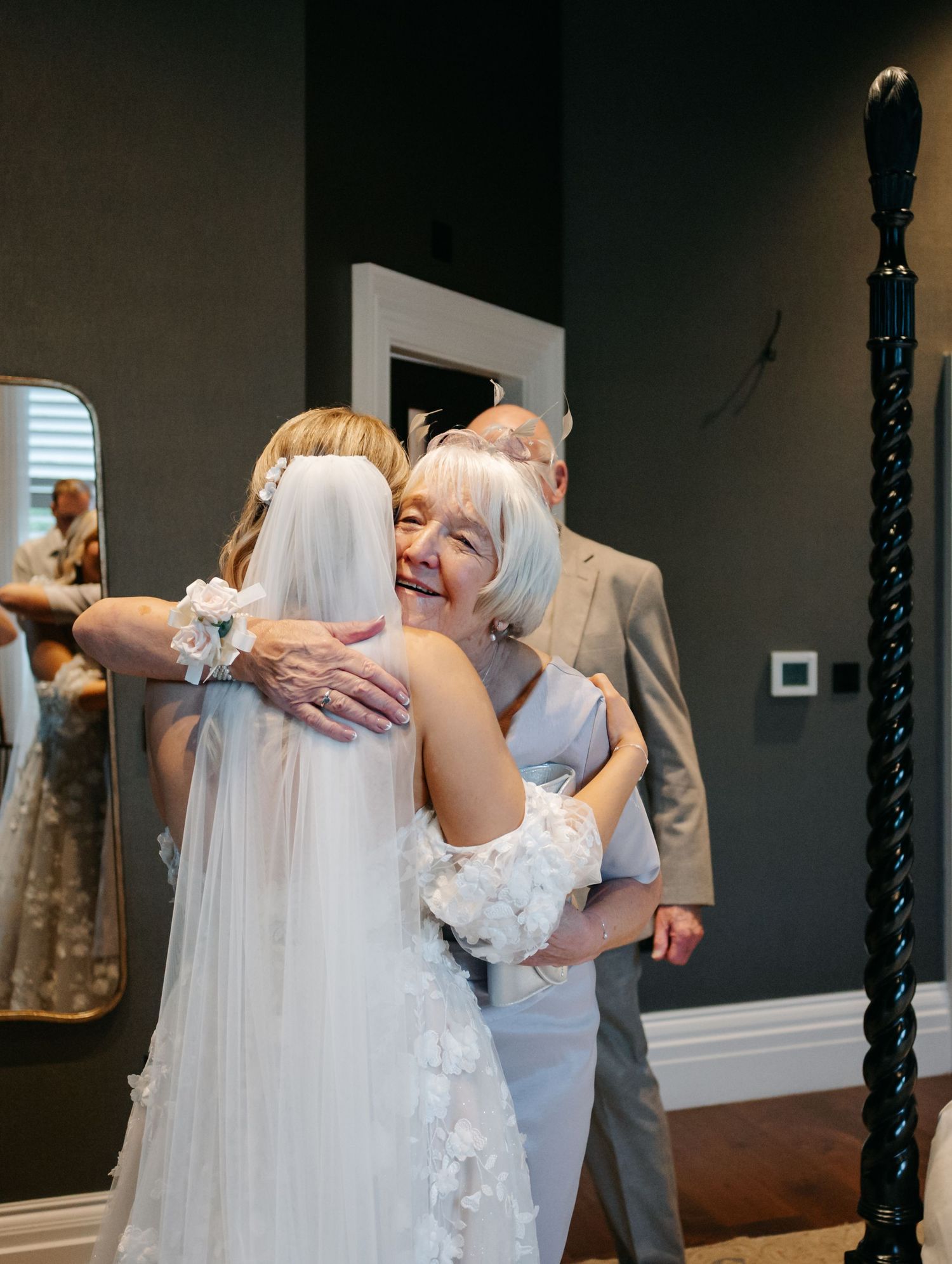 Two people share an emotional embrace during a wedding ceremony in a room with dark walls and hardwood floors.