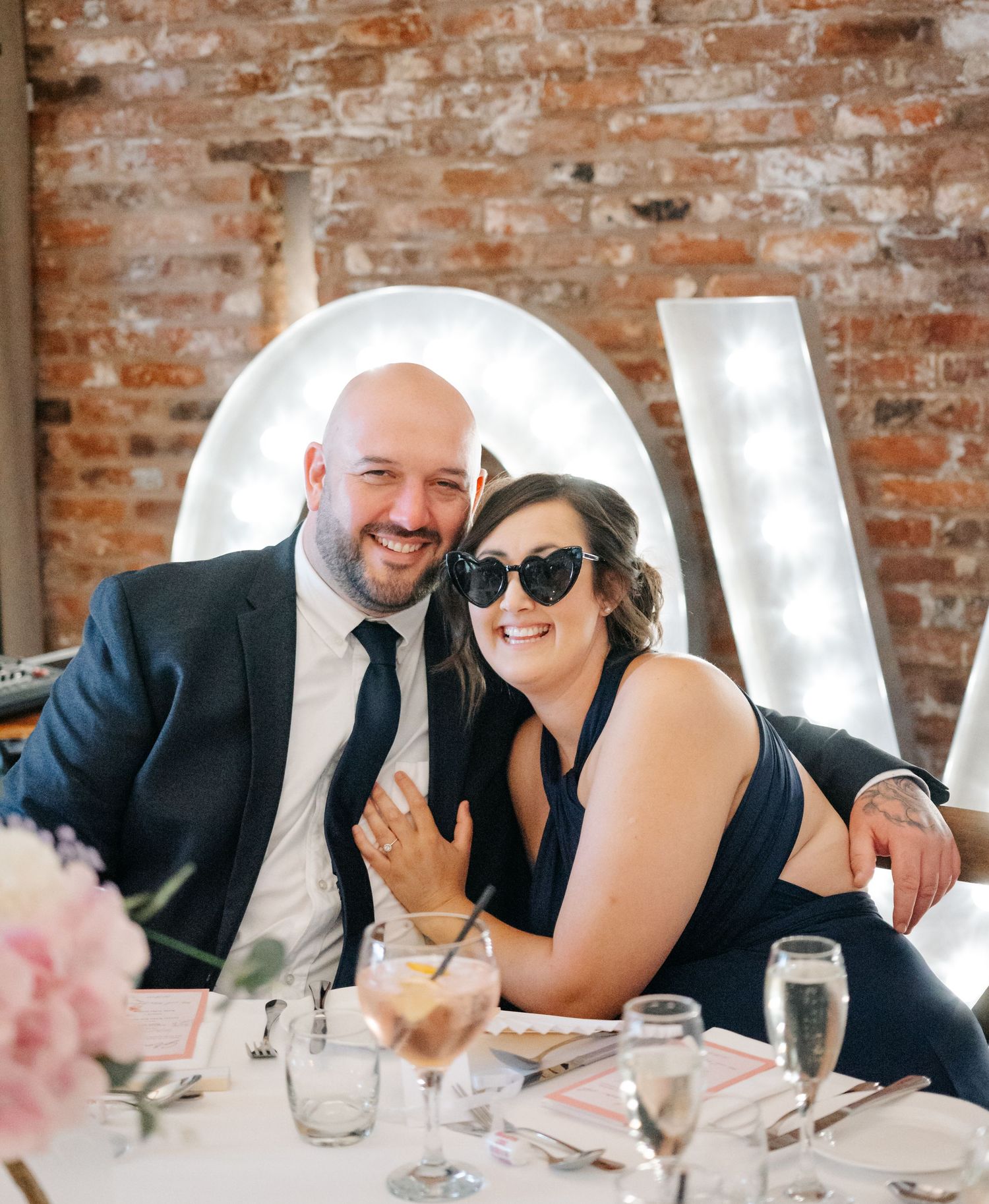 Wedding reception guests enjoying a meal at decorated tables with illuminated letters in background.