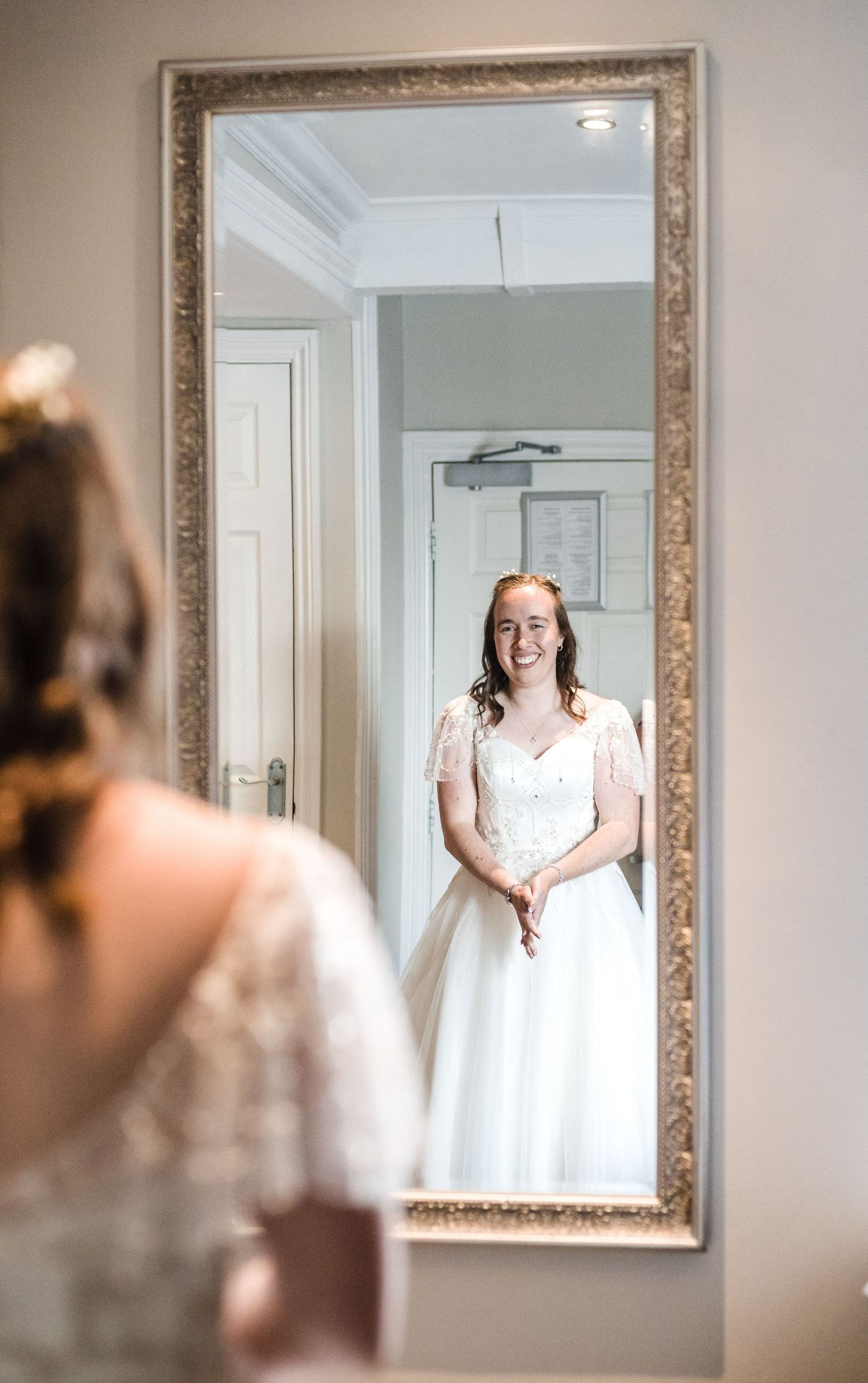 A reflection in an ornate mirror shows someone in a classic white wedding dress.
