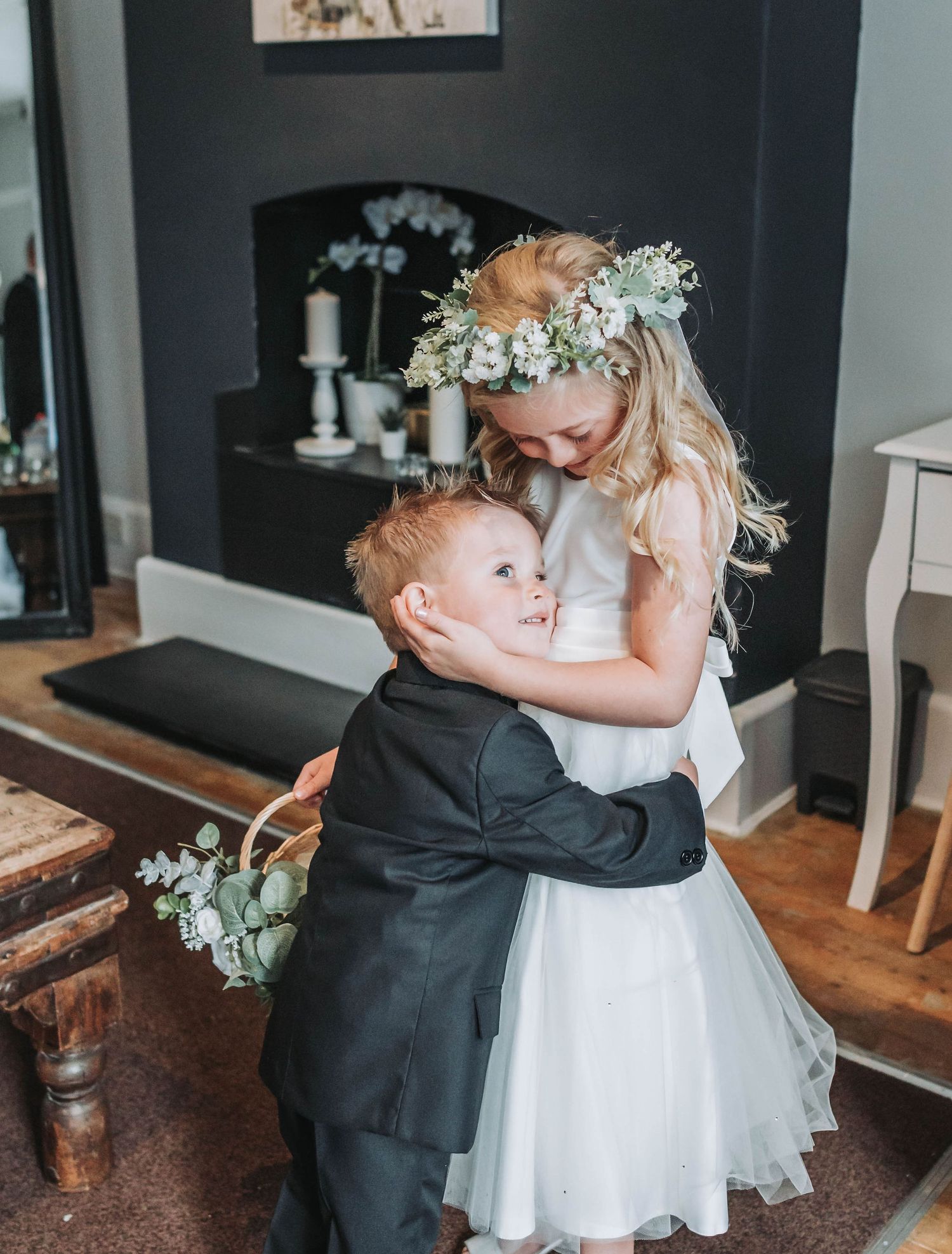 A flower girl in white dress and young ring bearer in tux share a sweet moment at a wedding.
