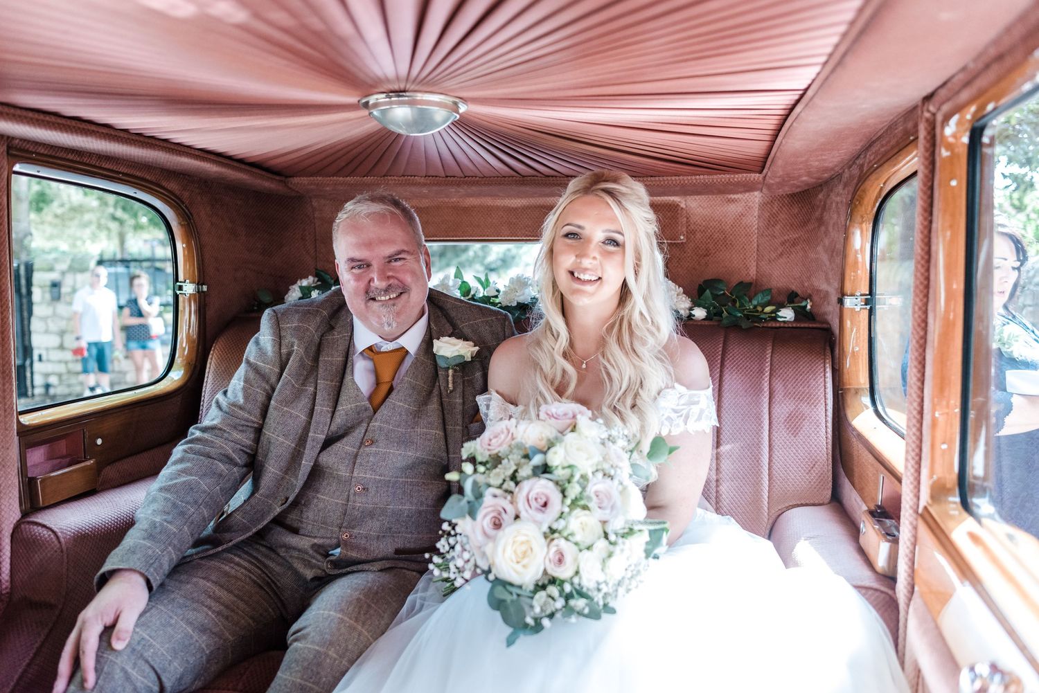 Interior of vintage car with pink fabric ceiling and wedding couple seated inside.