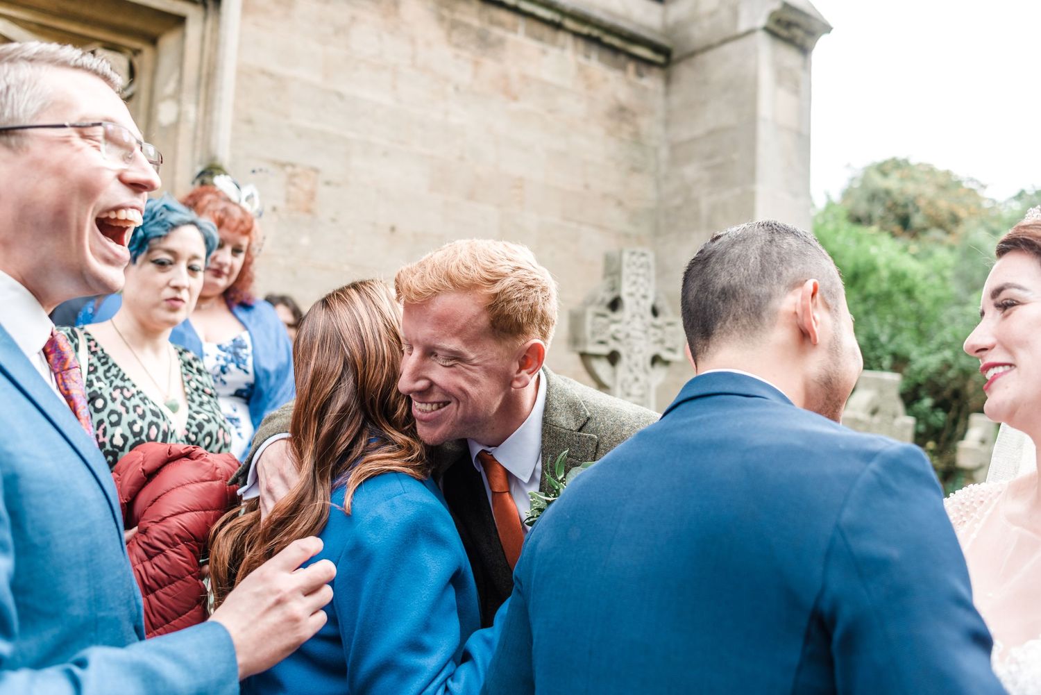 Wedding guests laugh and celebrate during outdoor reception by stone church.