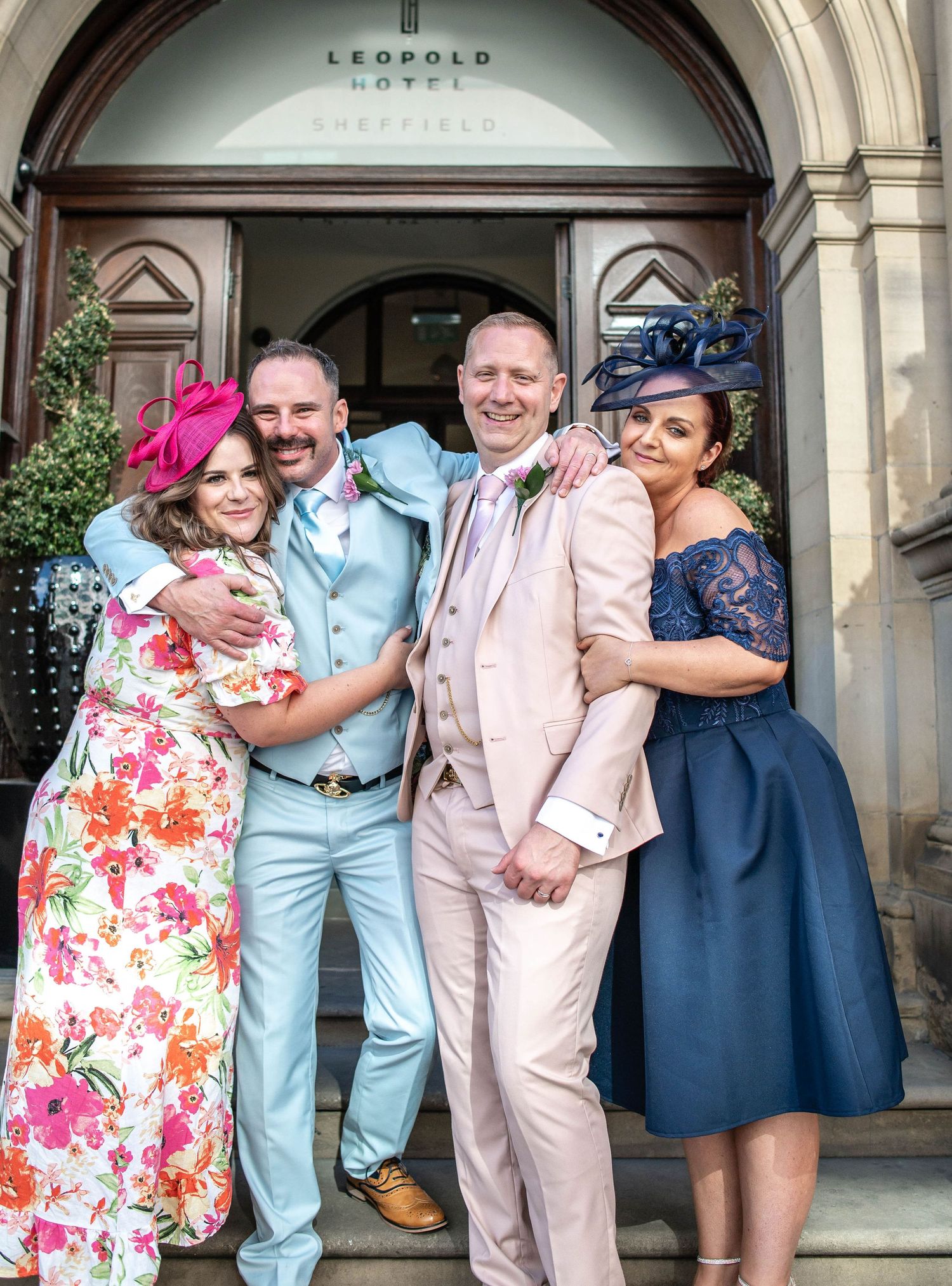 Wedding party in colorful formal attire posing together on hotel steps.