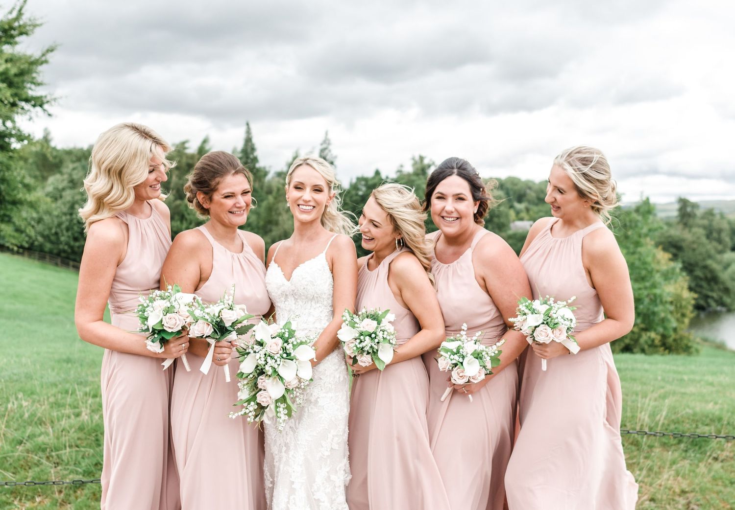 Bridal party in blush pink dresses pose outdoors with white bouquets.