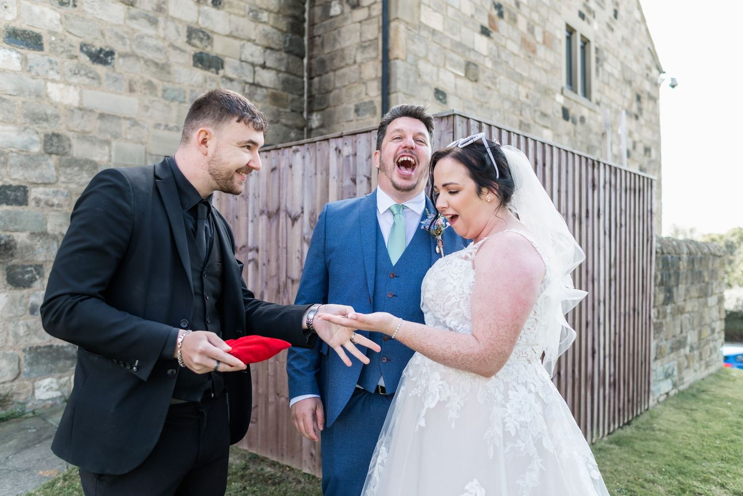 Candid laughing moment captured during wedding celebrations outside stone building.