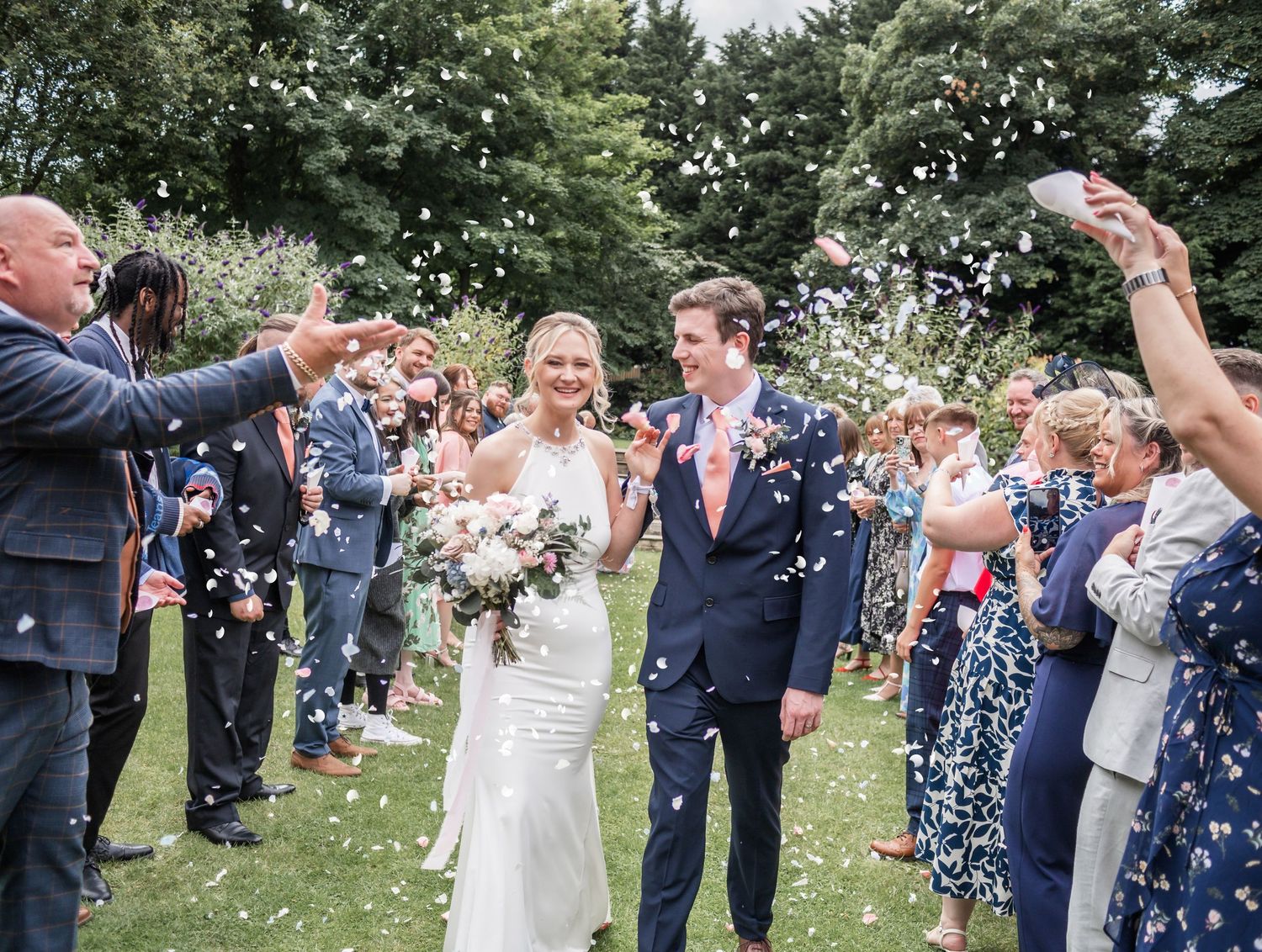Wedding couple walking through guest confetti shower during outdoor celebration.