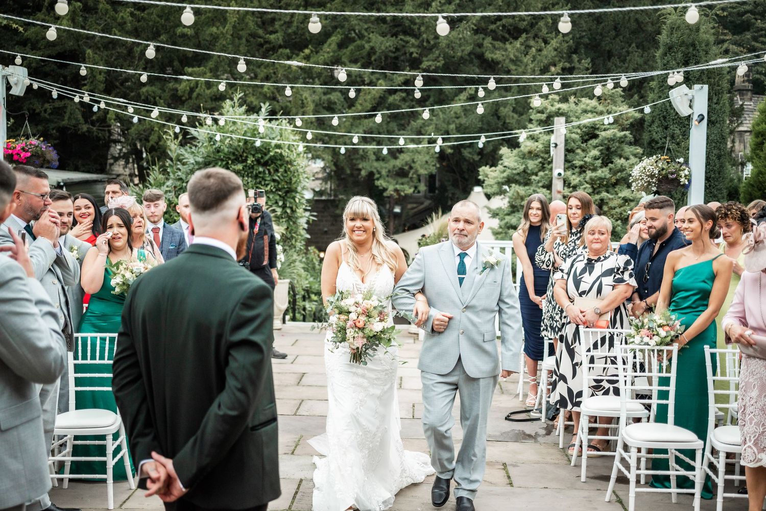 Joyful wedding ceremony exit under string lights with guests lined up on both sides.