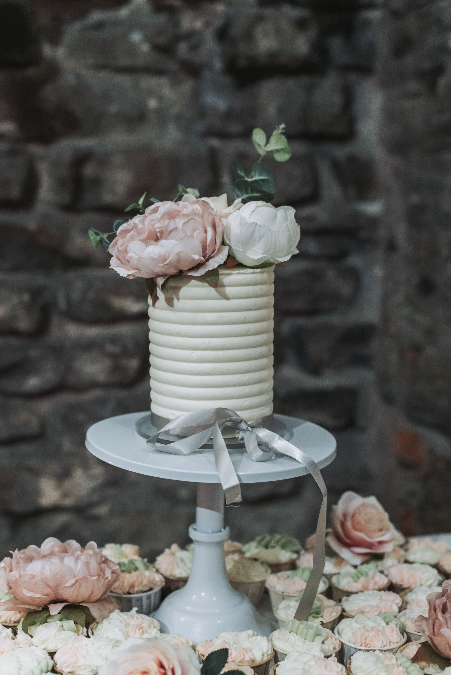 Simple white ribbed wedding cake decorated with blush pink roses on a white pedestal stand.
