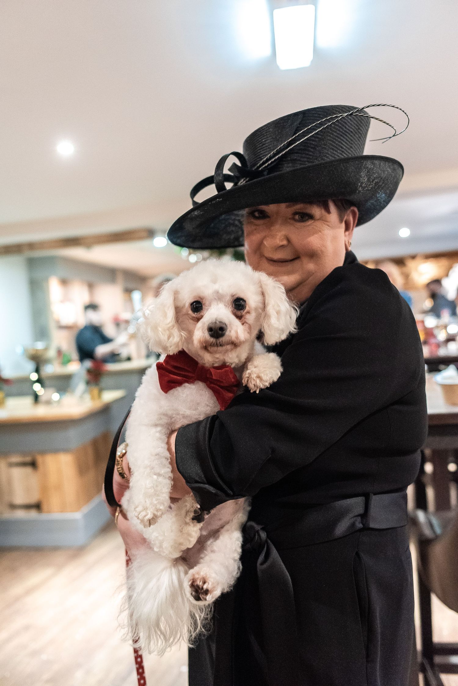 Small white dog wearing bow tie with companion at formal event.