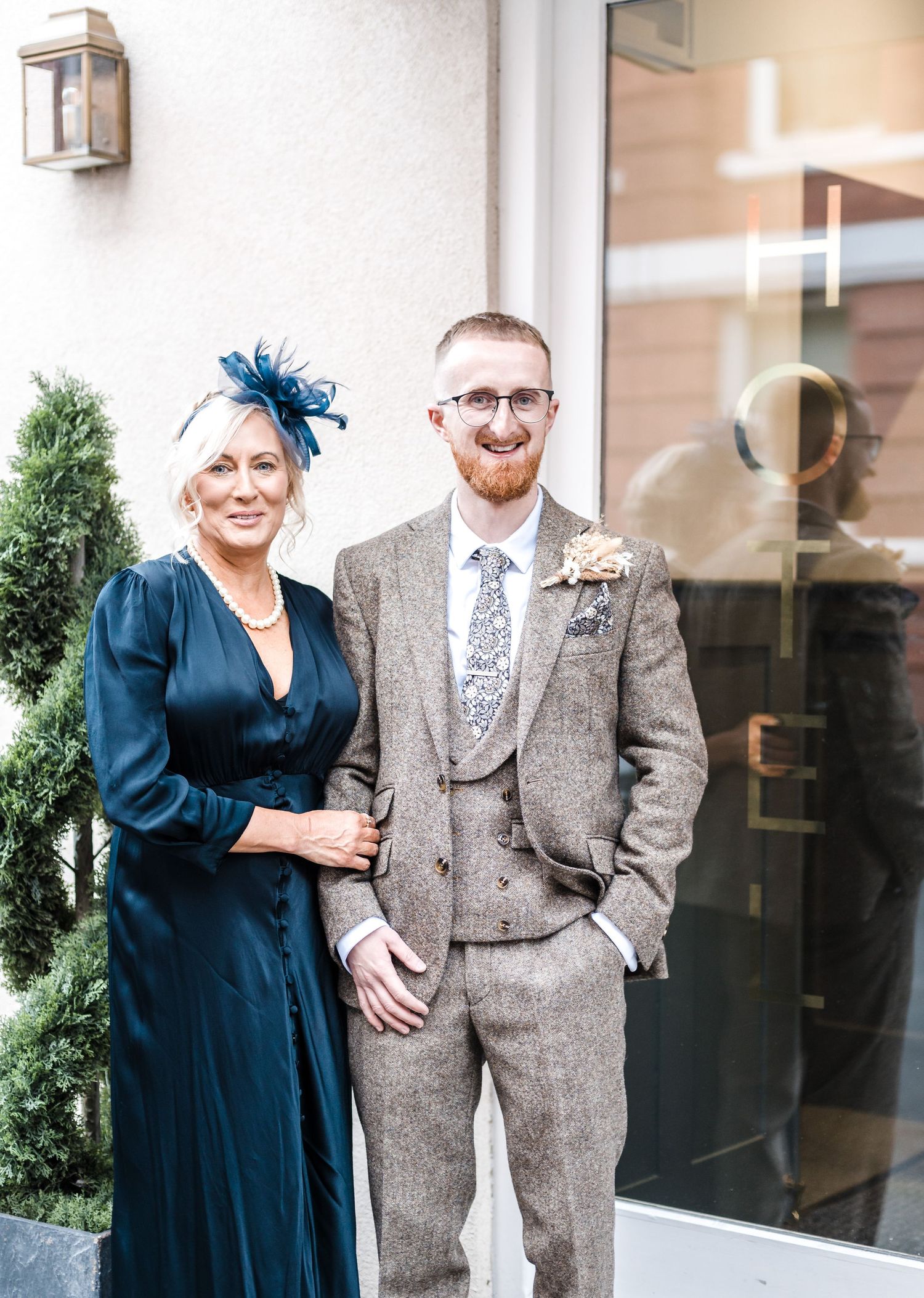 Wedding attendees in formal attire pose outside building with decorative lantern.