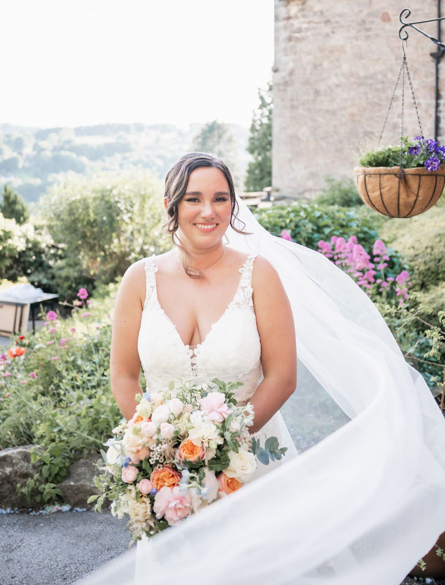 Elegant bridal portrait in garden setting with flowing veil and peach and white bouquet.