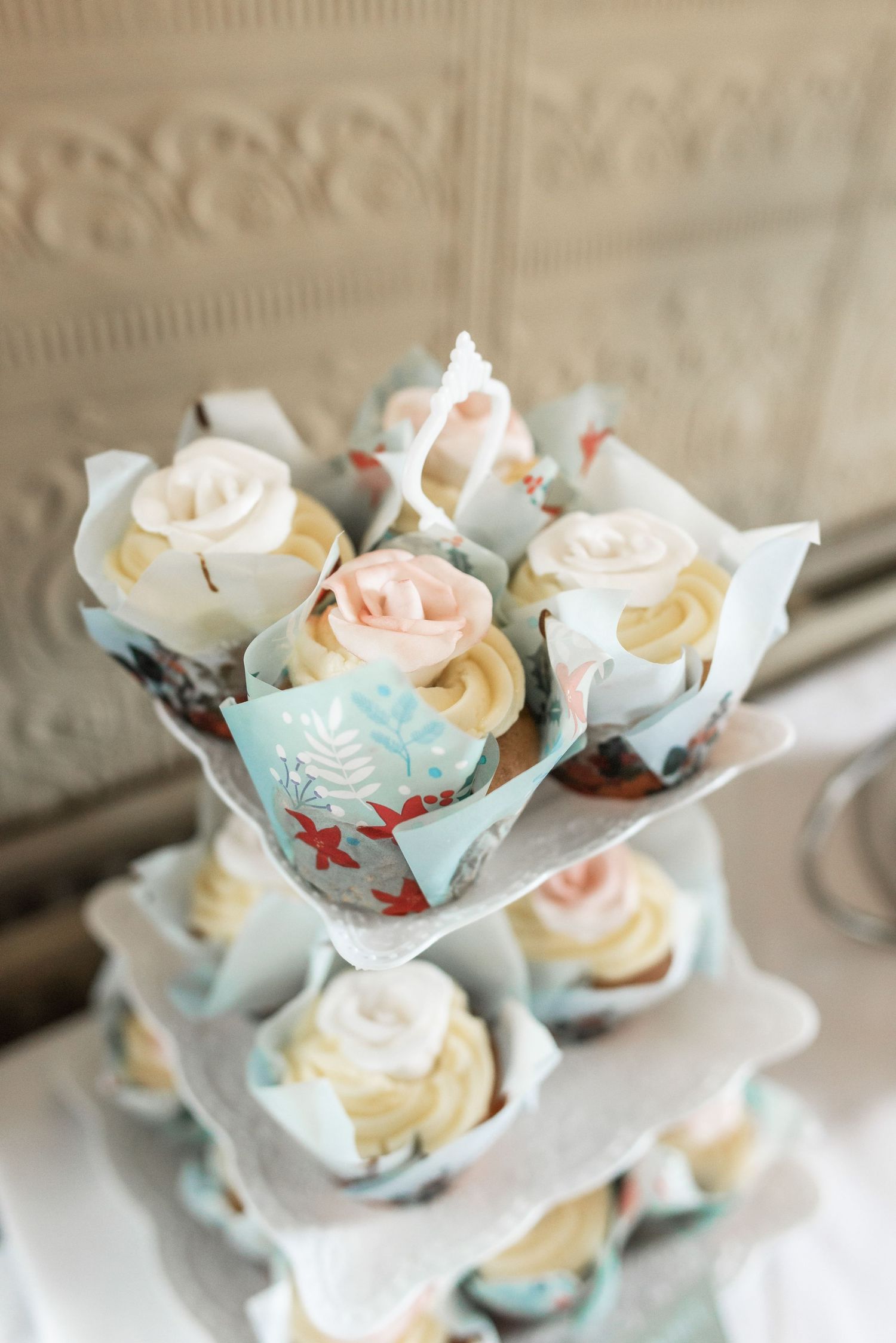 Delicate pastel cupcakes with rose frosting arranged on tiered display stand.