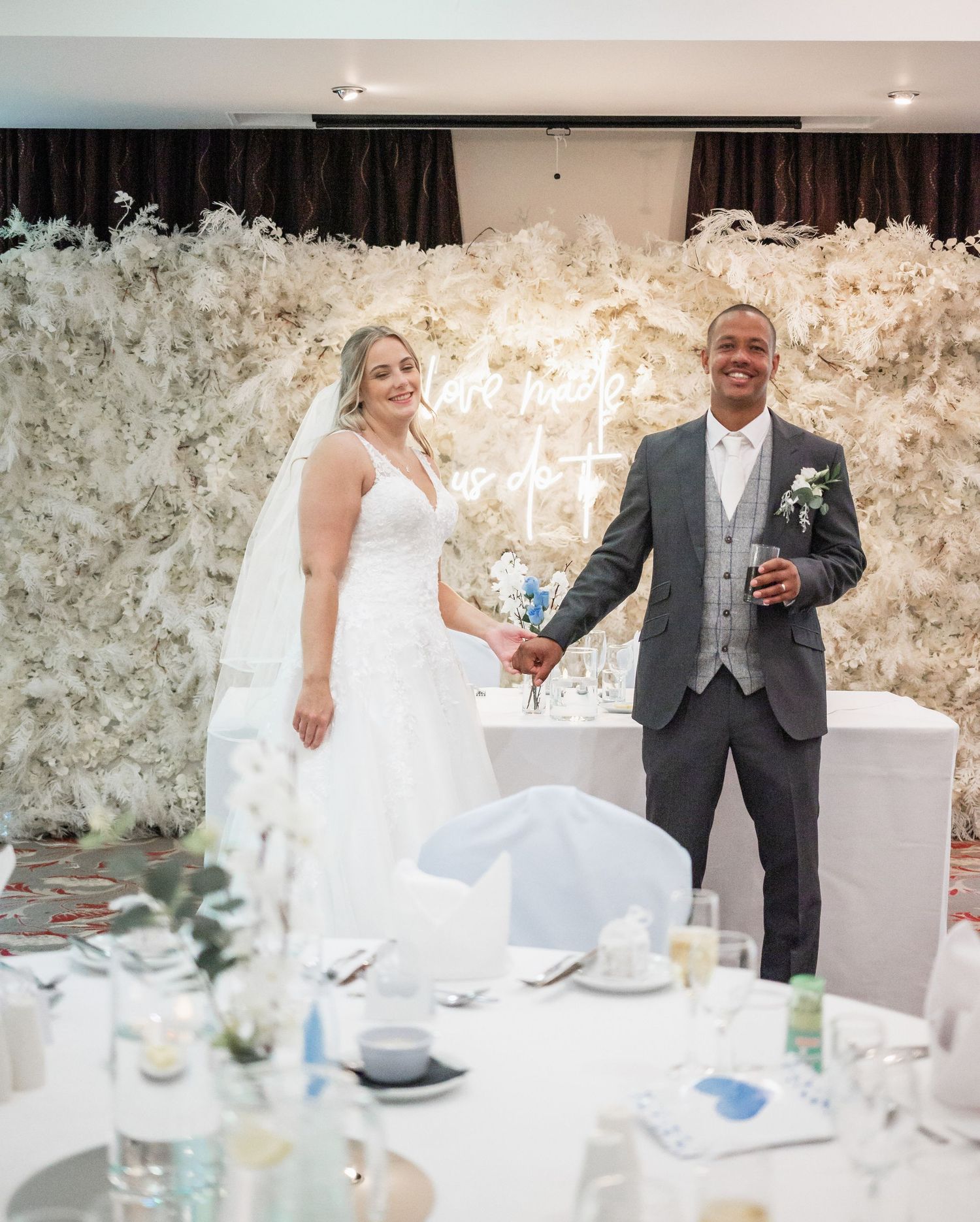 Wedding reception scene with a stunning white floral wall backdrop and elegant table settings.