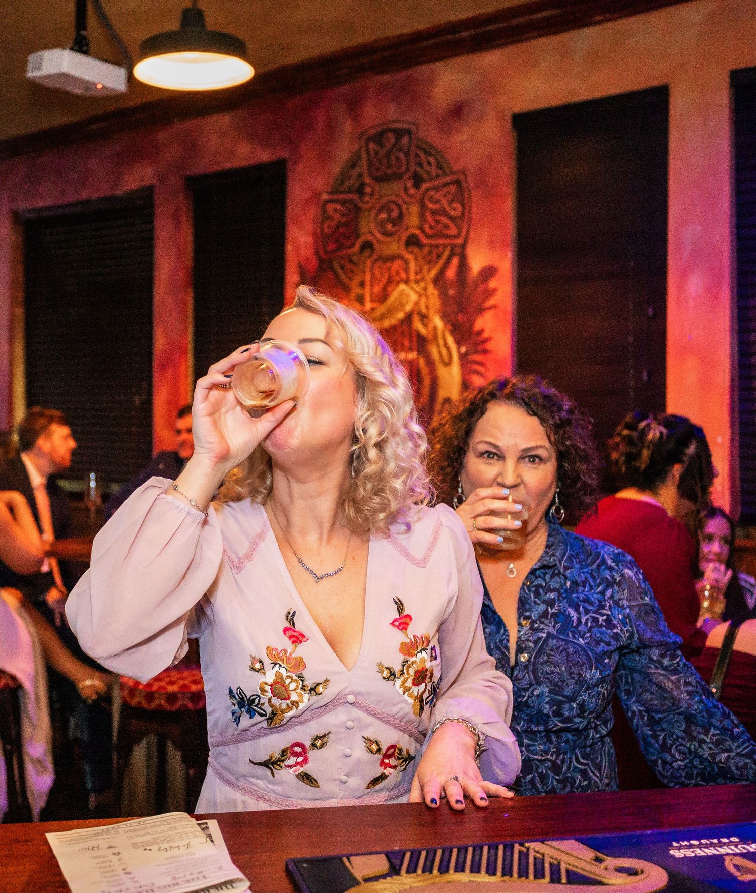 Two people enjoying drinks at bar with festive red lighting.
