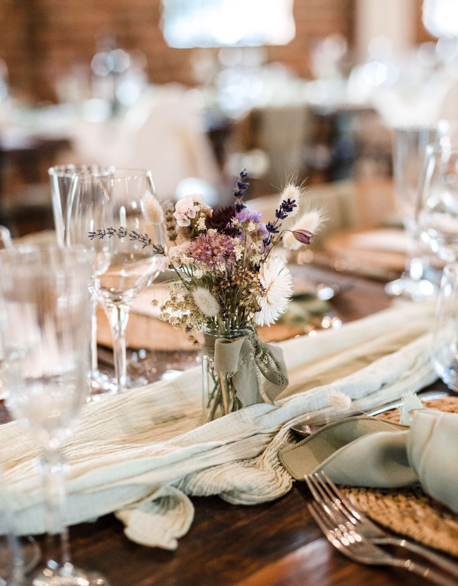 Elegant place setting with wildflower centerpiece and white table runner on wooden table.