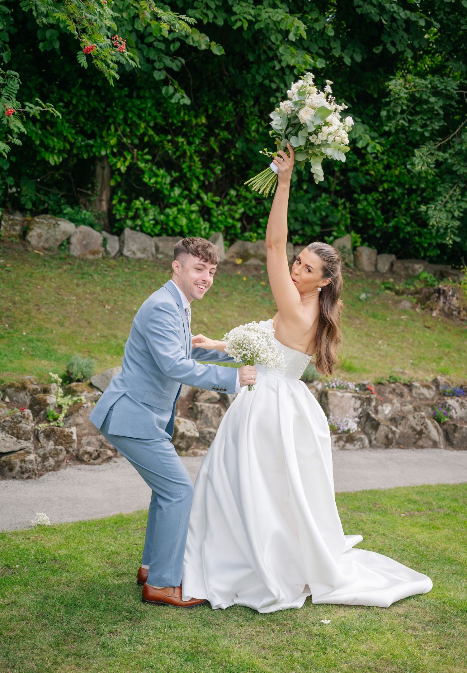 Wedding couple playfully posing on stone steps surrounded by lush greenery.