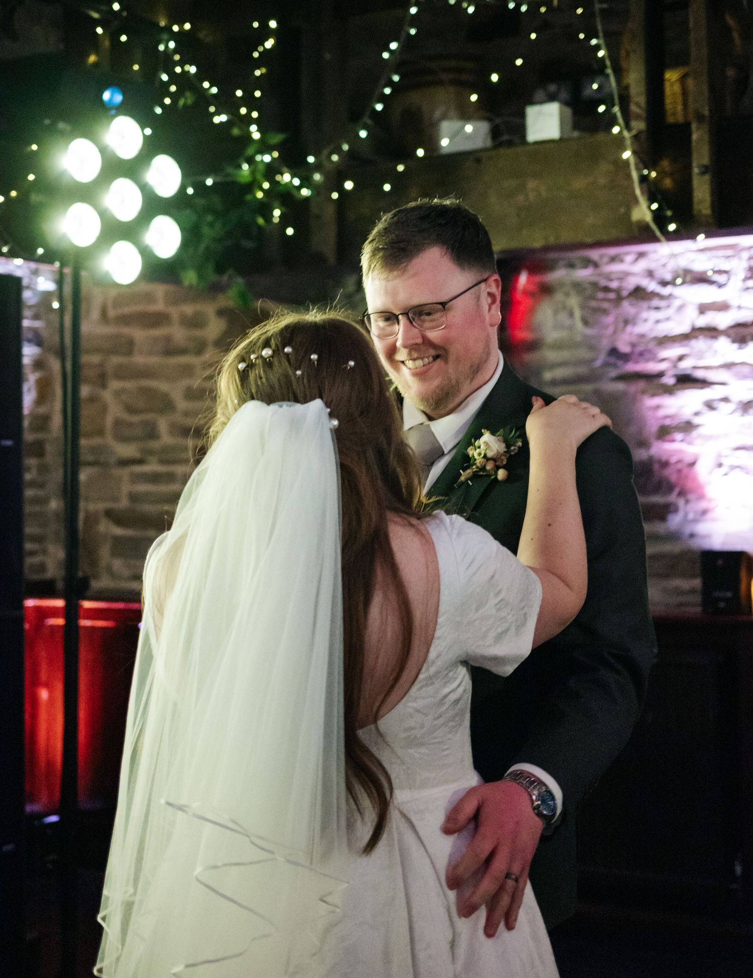 A couple shares their first dance under twinkling lights at an intimate indoor wedding reception.