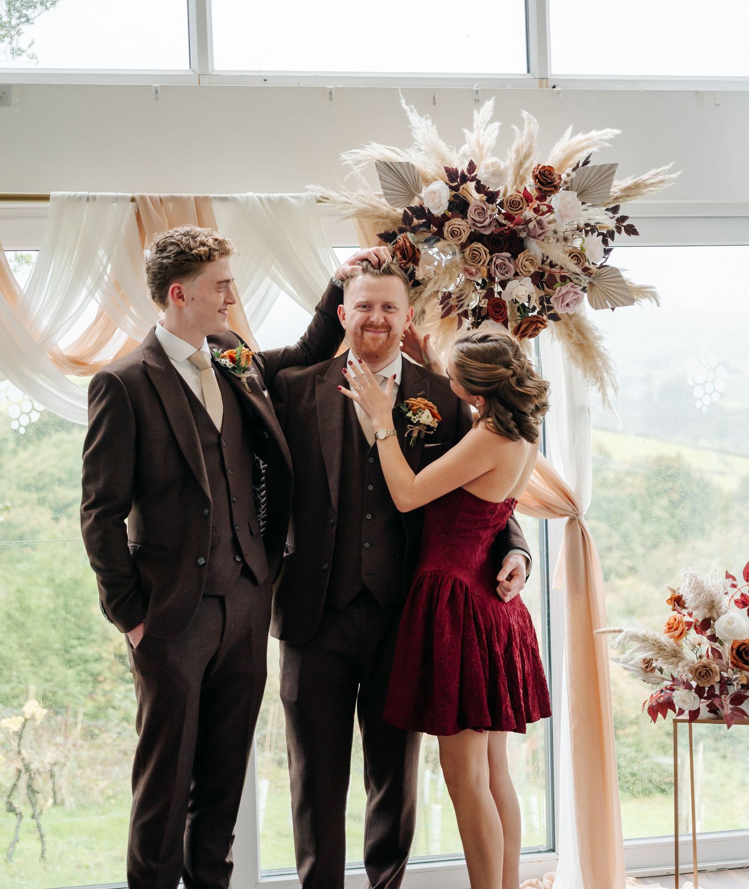 Wedding party celebrates with joyful expressions in a bright indoor venue with decorative floral elements.