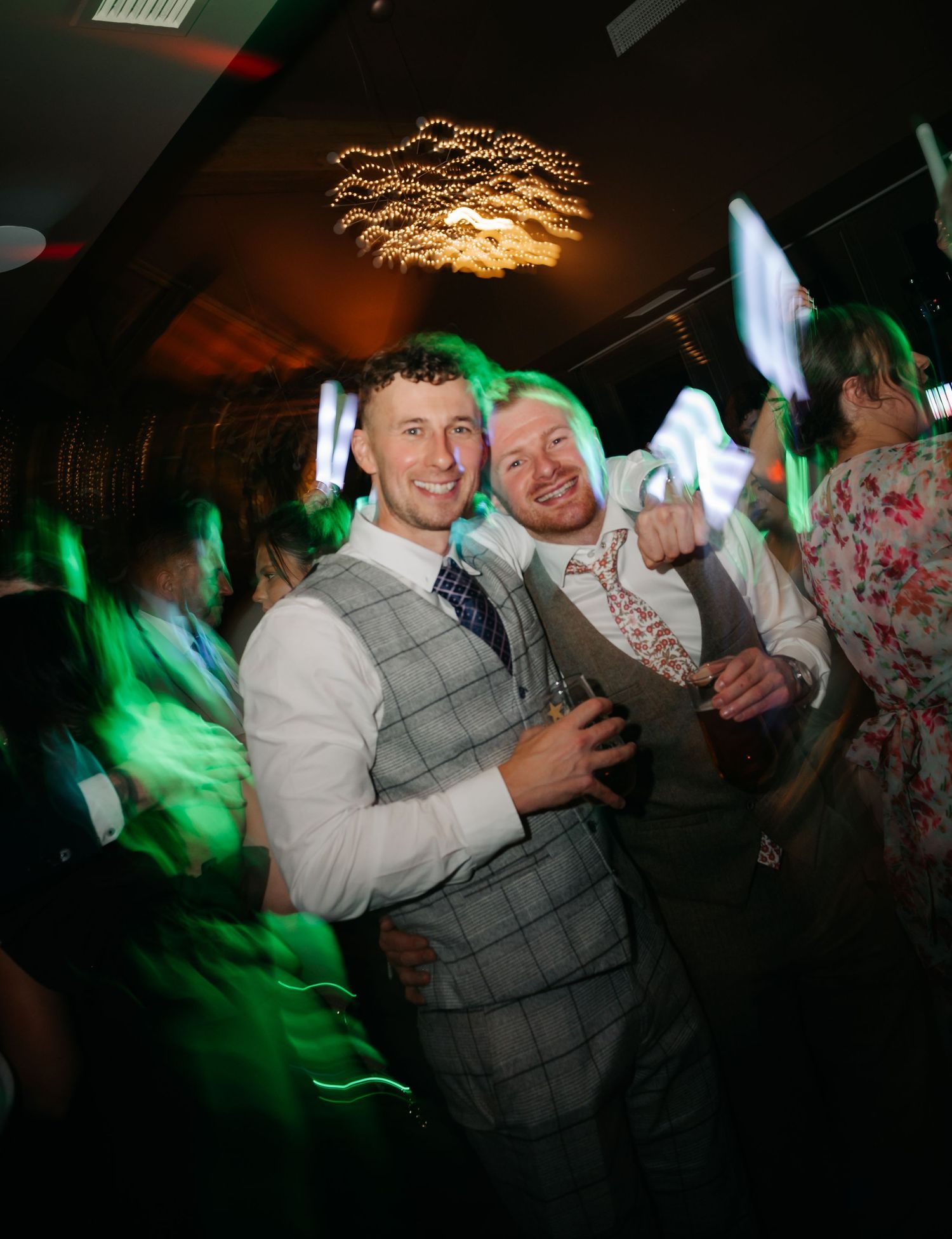 Dance floor celebration at a wedding reception with green lighting effects and festive atmosphere.