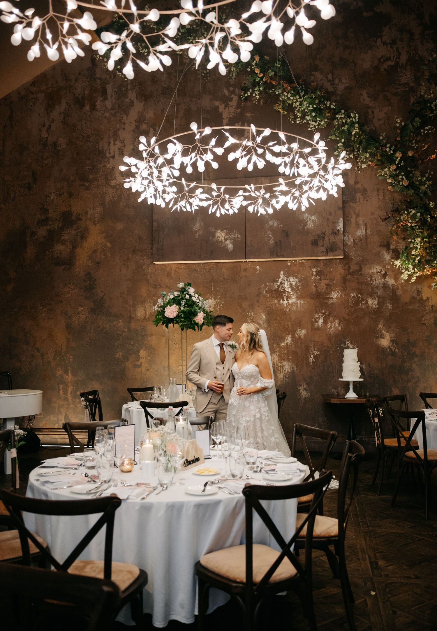 Reception venue with round tables, white linens, and glowing leaf-pattern ceiling lights.